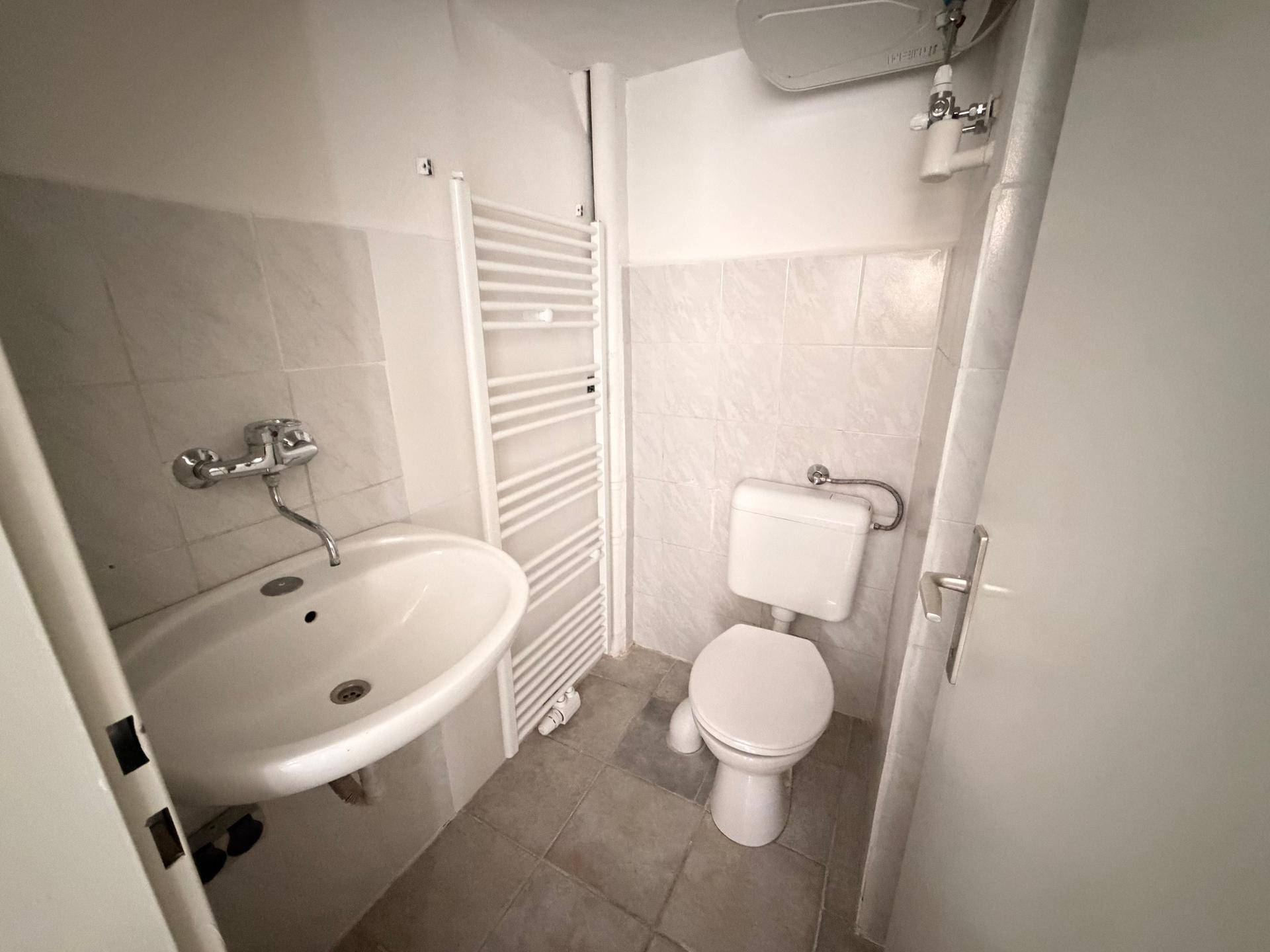 Kleines Badezimmer mit Waschbecken, Toilette und praktischem Handtuchheizkörper.