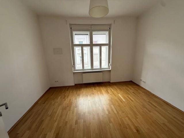 Leerer Raum mit hellem Parkettboden und großem Fenster, bereit zur individuellen Gestaltung.