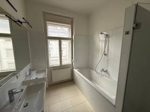 Badezimmer mit Doppelwaschbecken, Badewanne und Fenster für natürliche Belüftung.