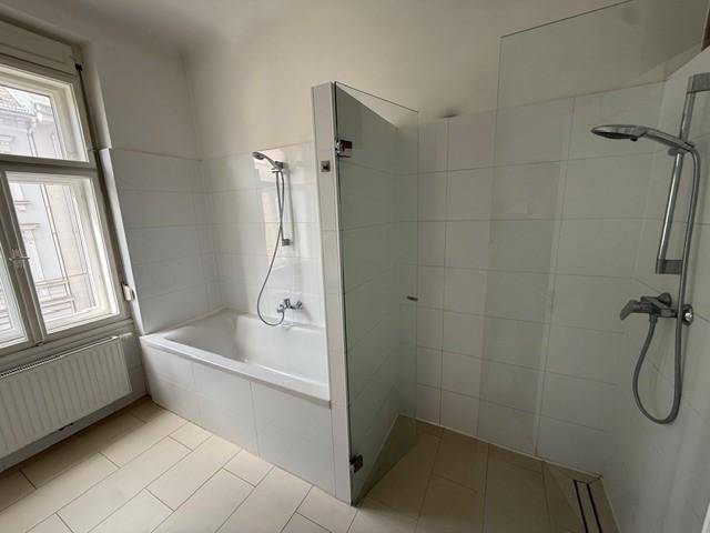 Badezimmer mit Badewanne, separater Dusche und Fliesenboden in neutralen Farben.