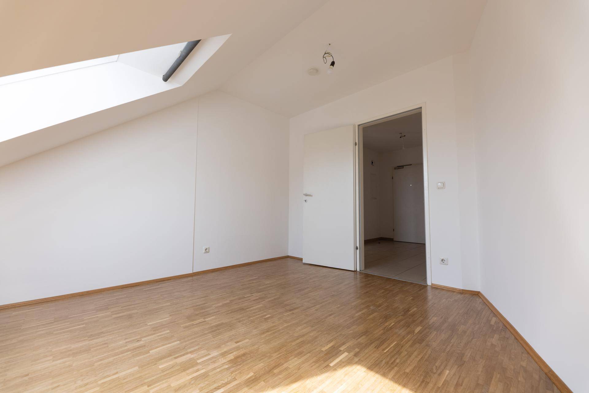 Leeres Zimmer mit Parkettboden und weiß gestrichenen Wänden.