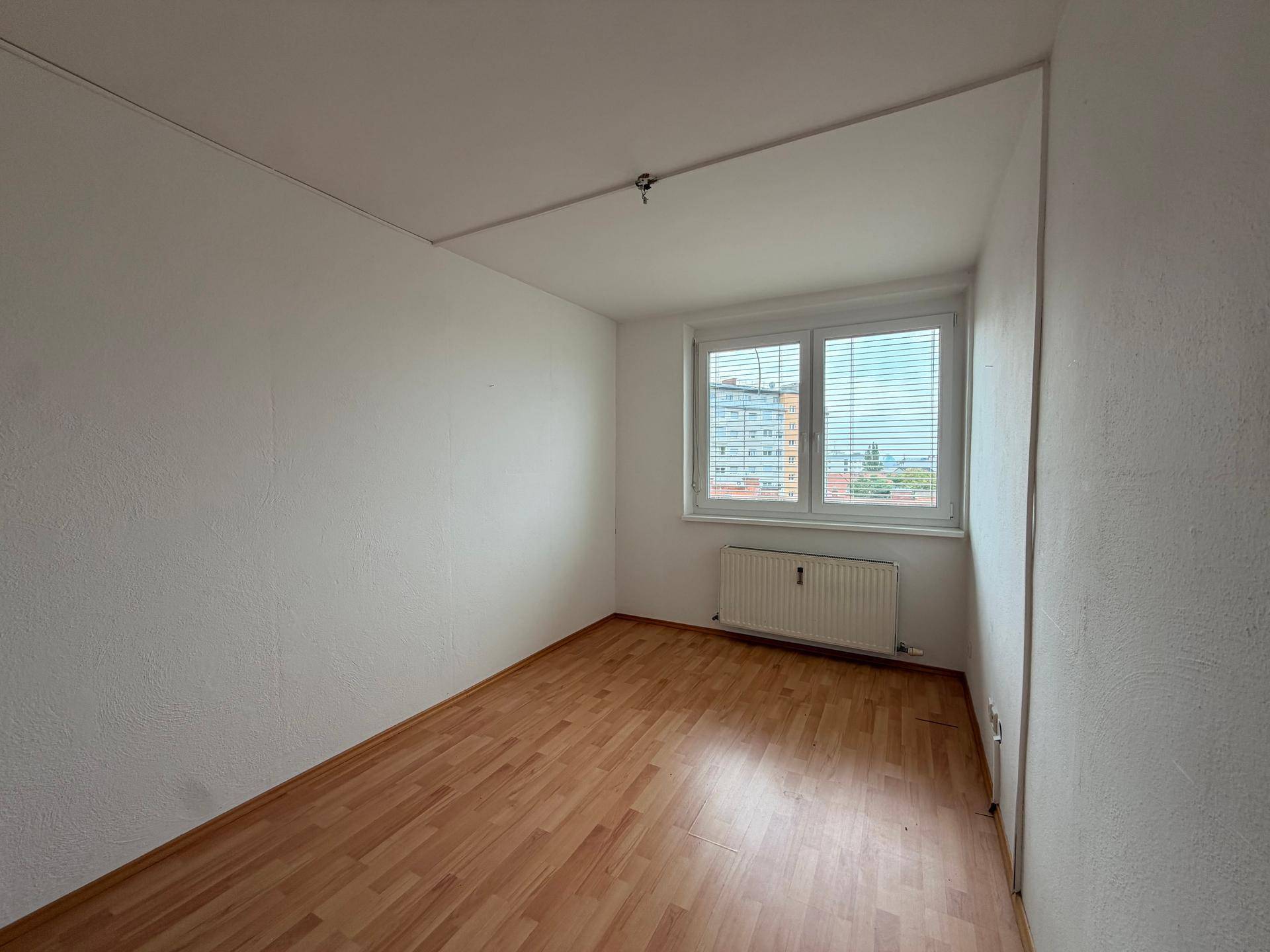 Helles Schlafzimmer mit Parkettboden und Fenster mit Blick auf die Umgebung.