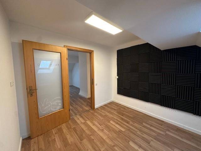 Zimmer mit Holzboden, einer Tür mit Milchglas und einer Wand mit schwarzen Schallschutzplatten.