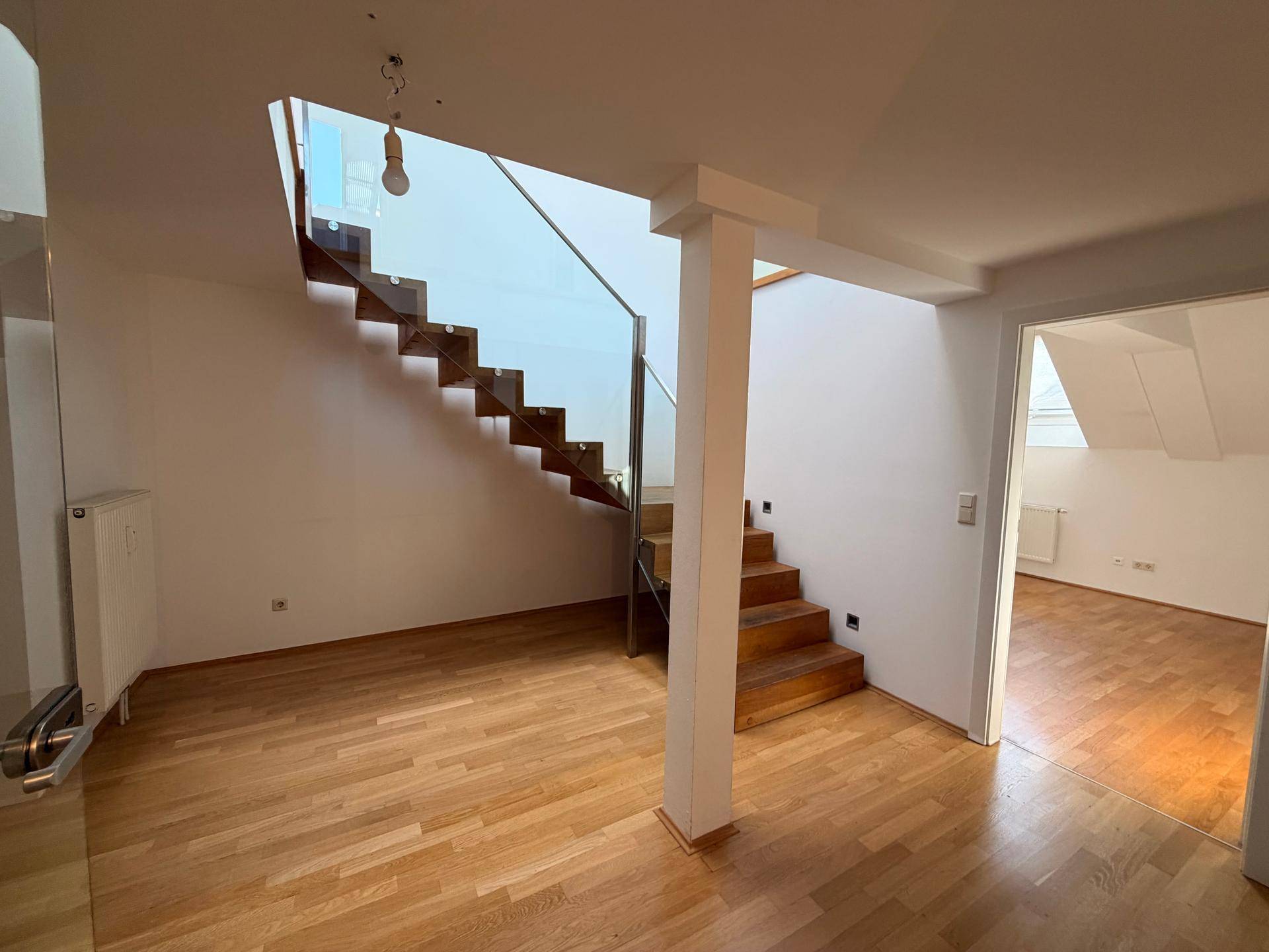 Geräumiger Wohnbereich mit Holzboden und eleganter Treppe mit Glasgeländer.