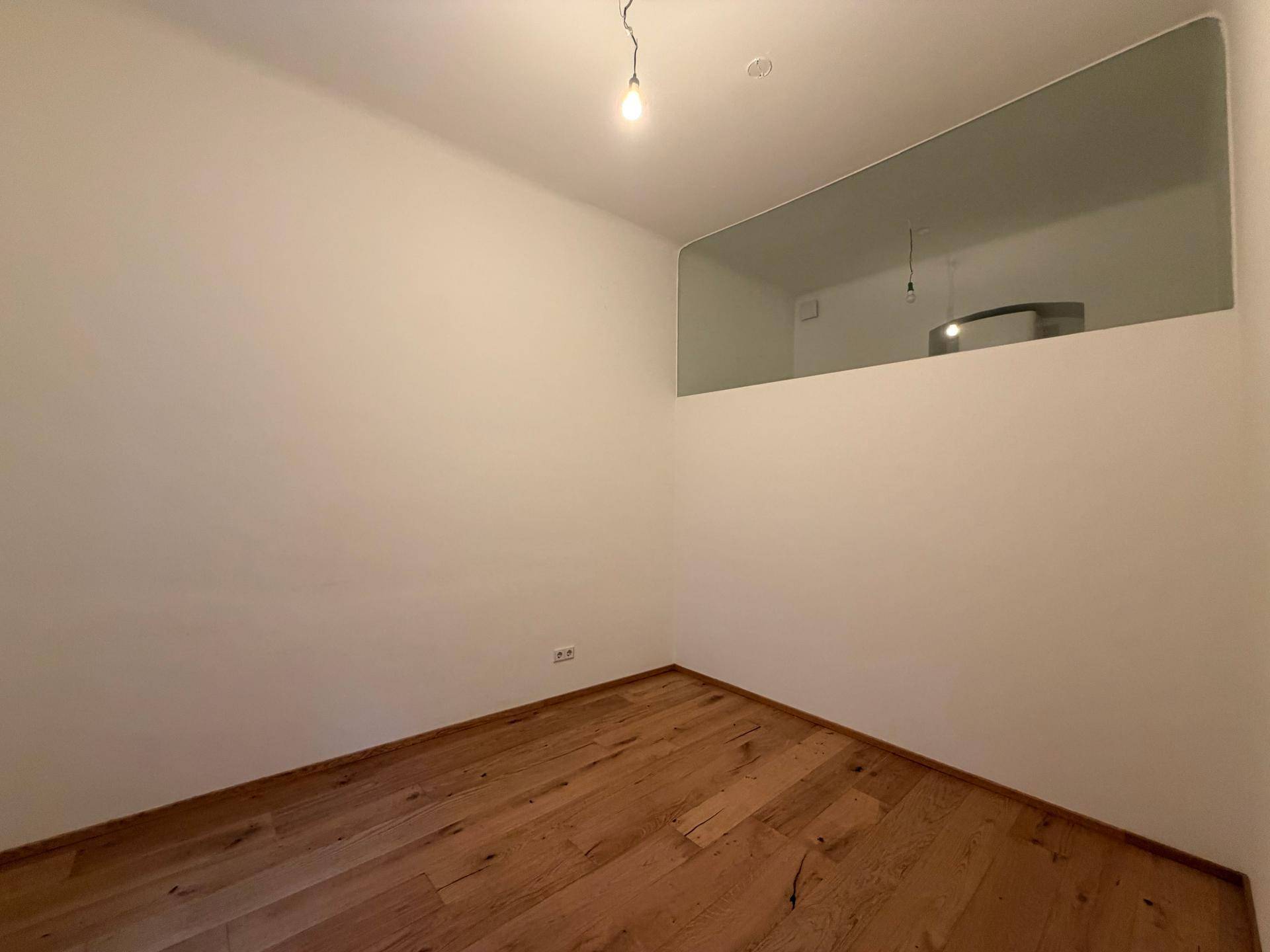 Leerer Raum mit Holzboden und einer oberen Glaswand, die Licht durchlässt.