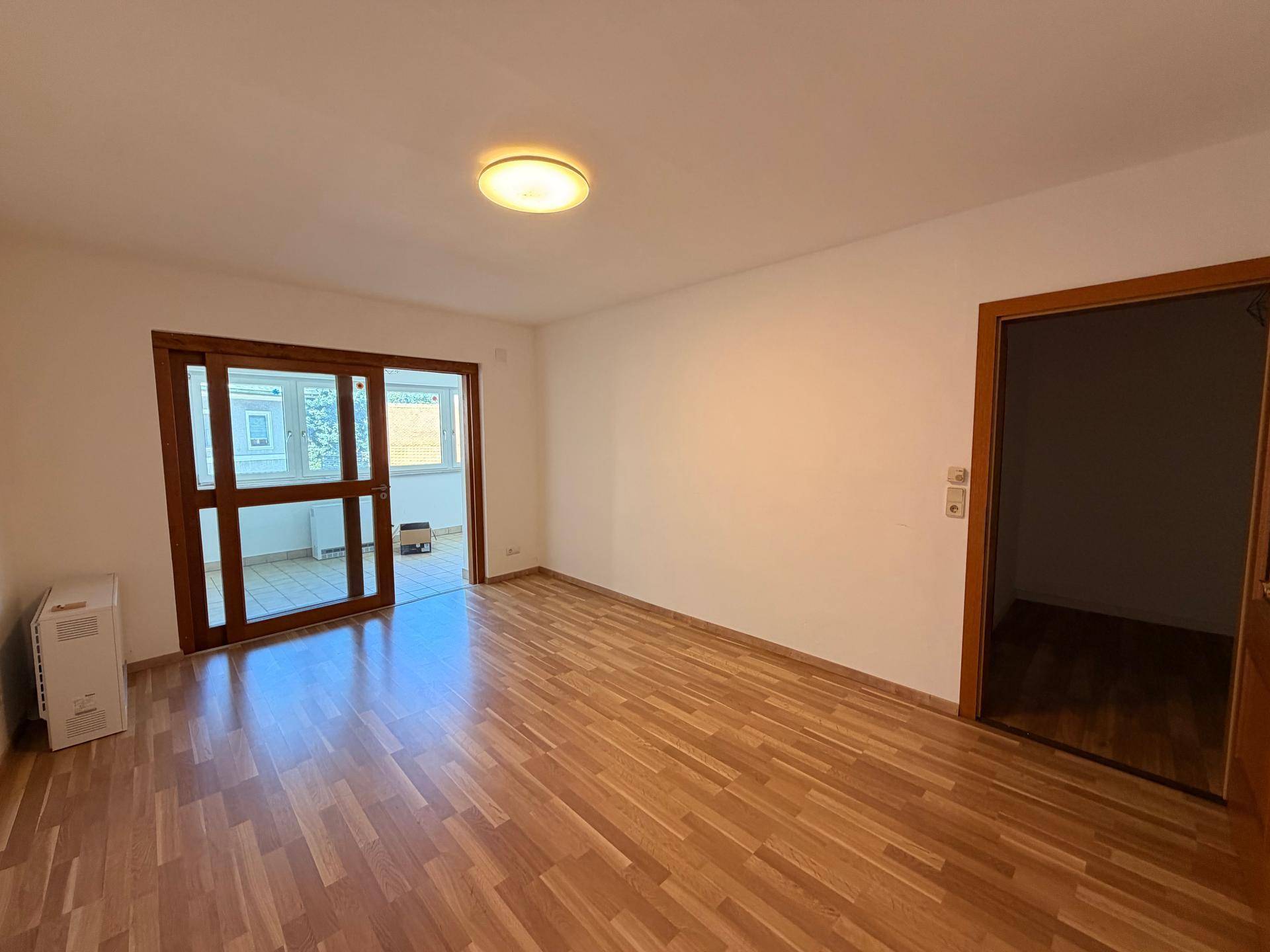 Geräumiger Wohnbereich mit Laminatboden und Schiebetüren, die zu einem weiteren Raum führen.
