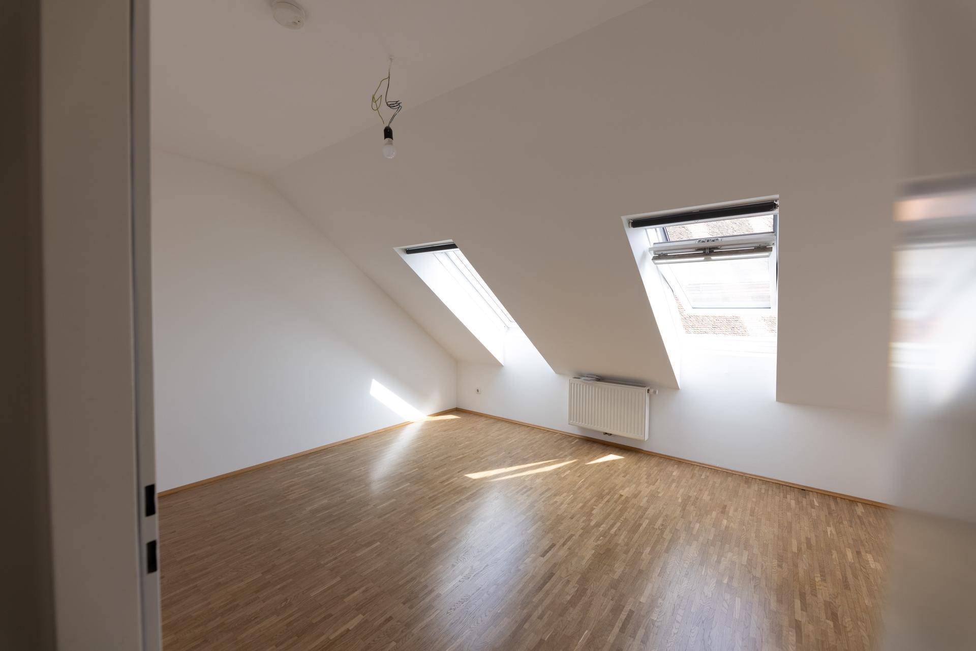 Lichtdurchflutetes Zimmer mit Dachschrägen, Dachfenstern und Parkettboden.