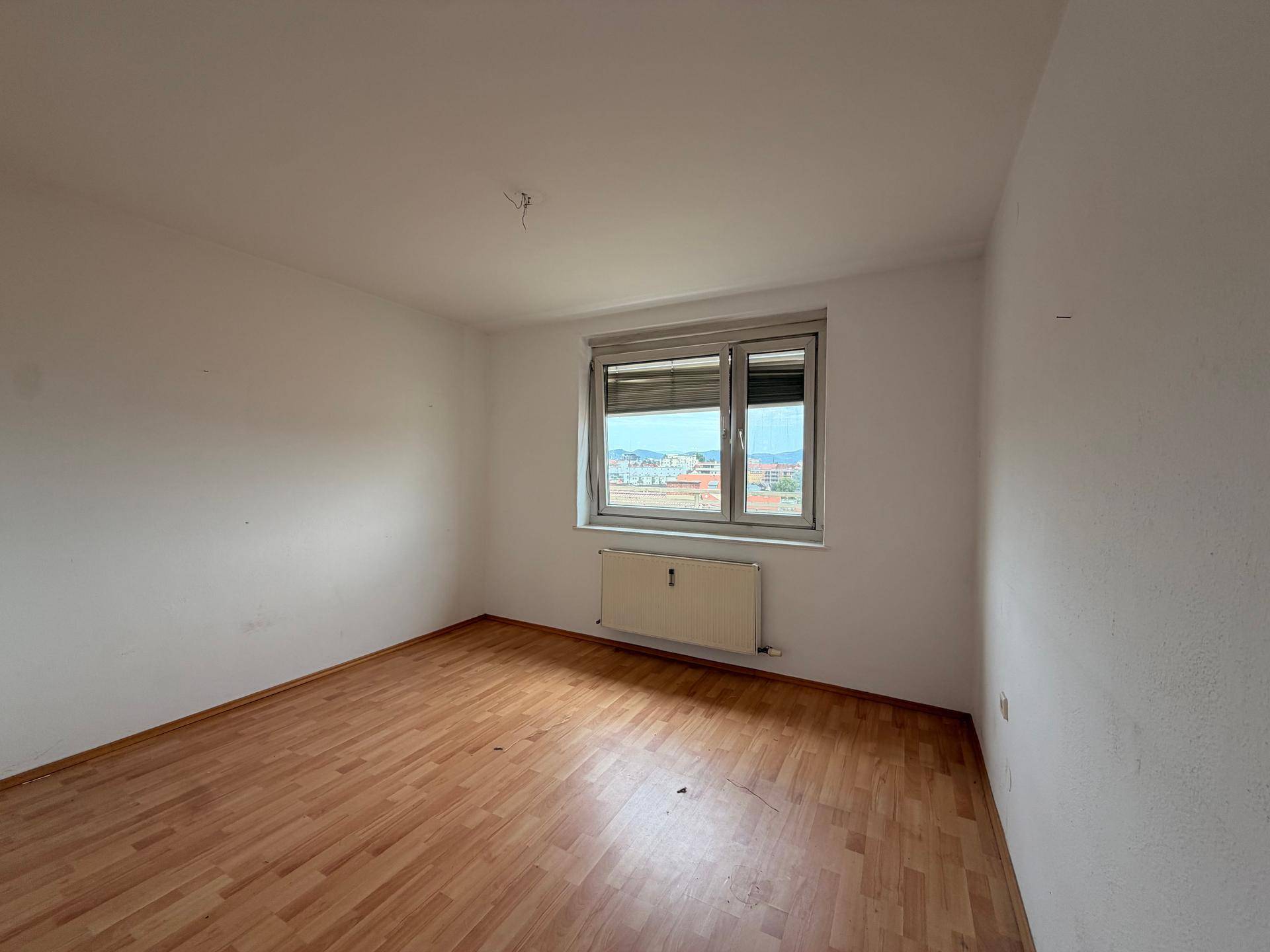 Helles Zimmer mit Parkettboden und Heizkörper unter dem Fenster mit Weitblick.
