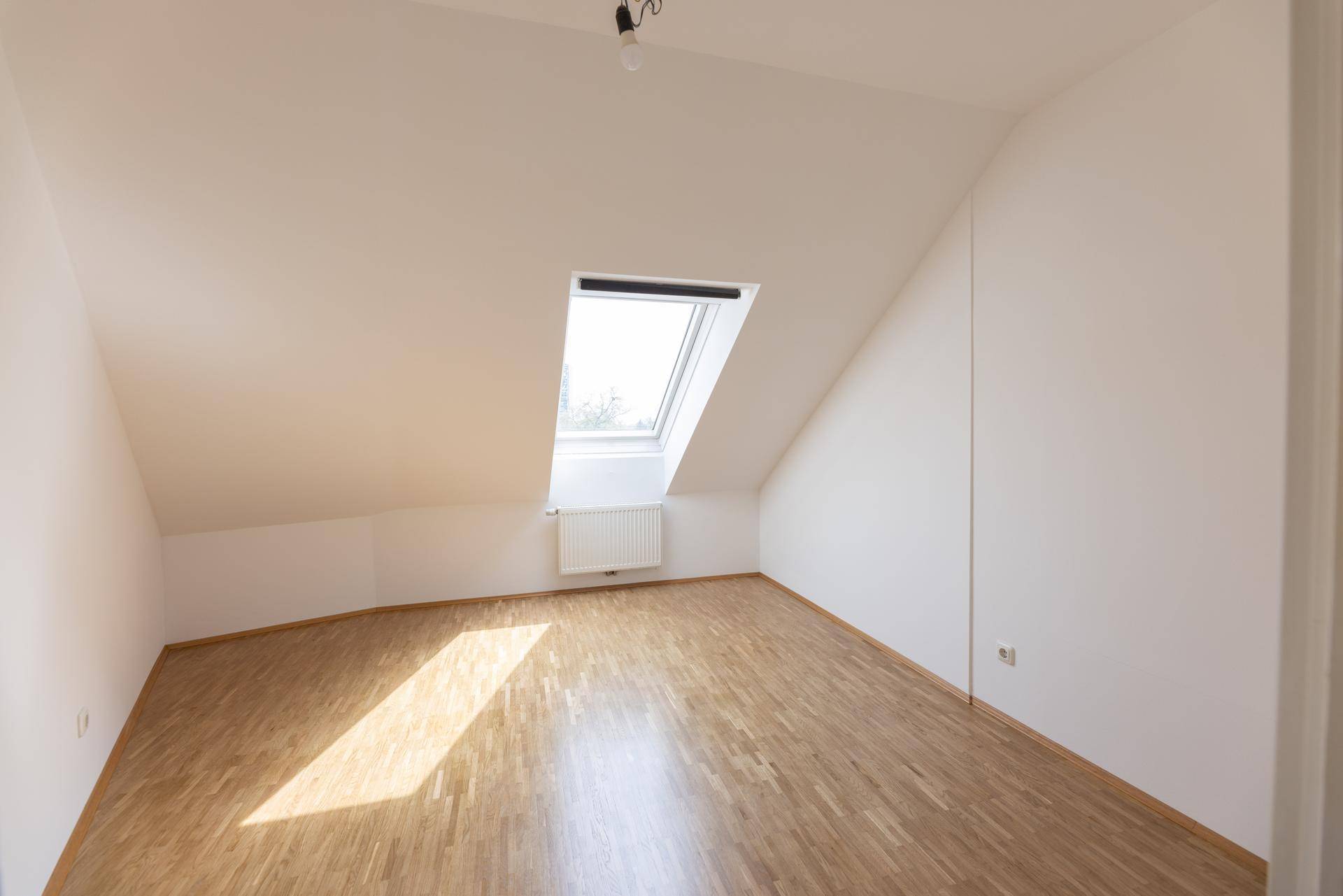 Helles Zimmer mit Dachschräge, einem Dachfenster und Parkettboden.