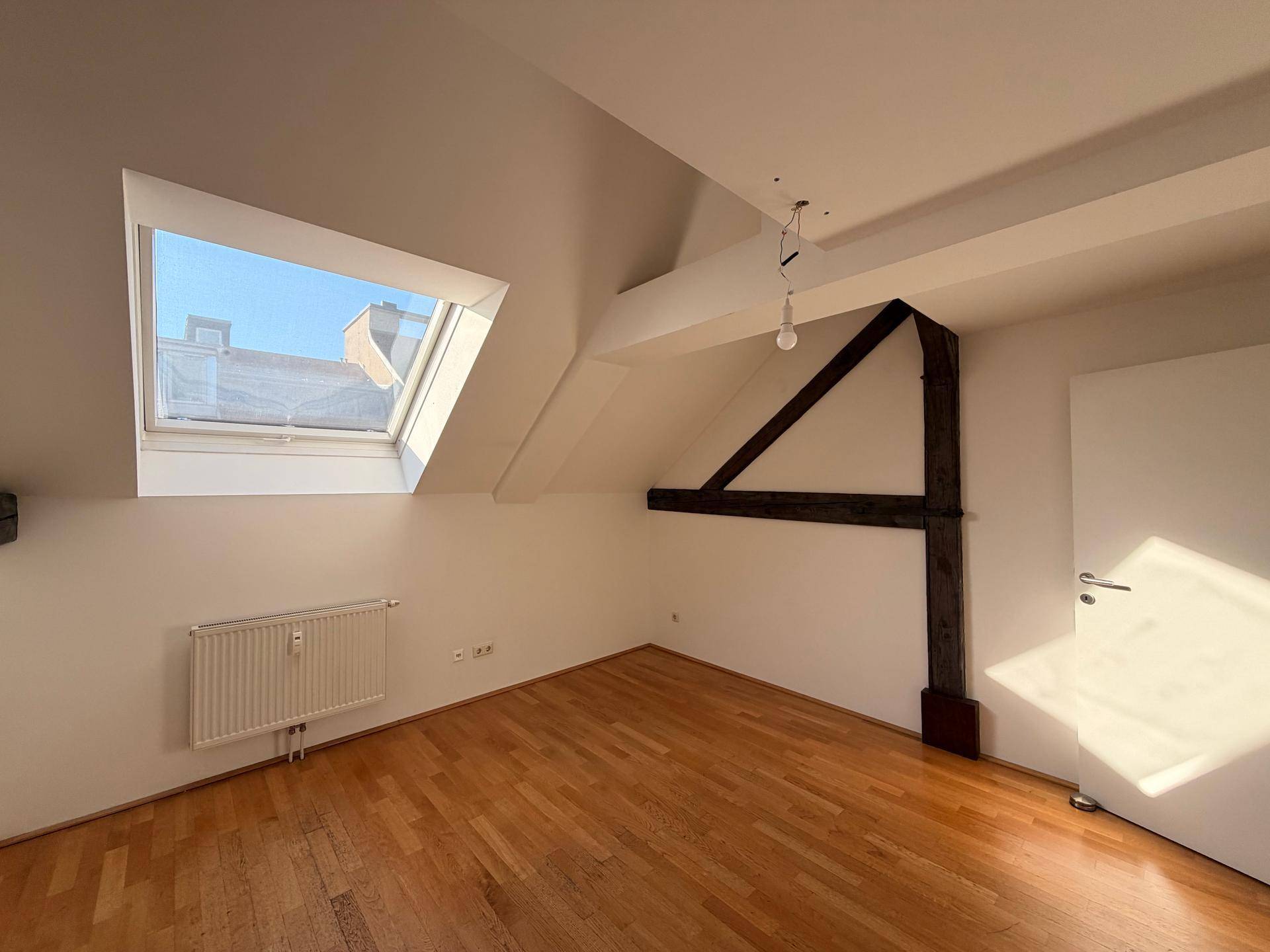 Gemütliches Schlafzimmer mit Holzboden, Dachfenster und rustikalem Holzbalken.