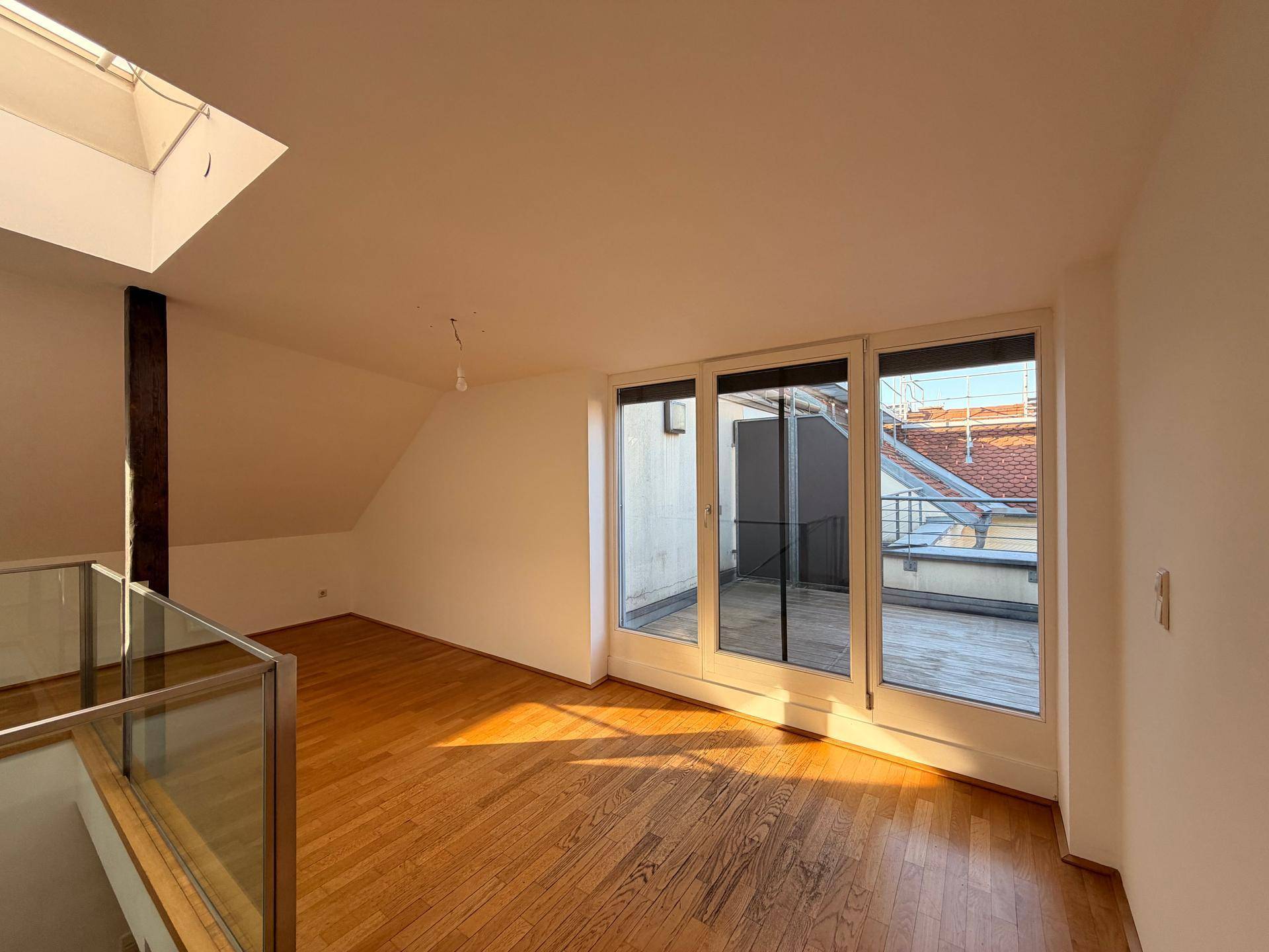 Lichtdurchfluteter Raum mit Holzboden und breitem Zugang zu einer sonnigen Dachterrasse.