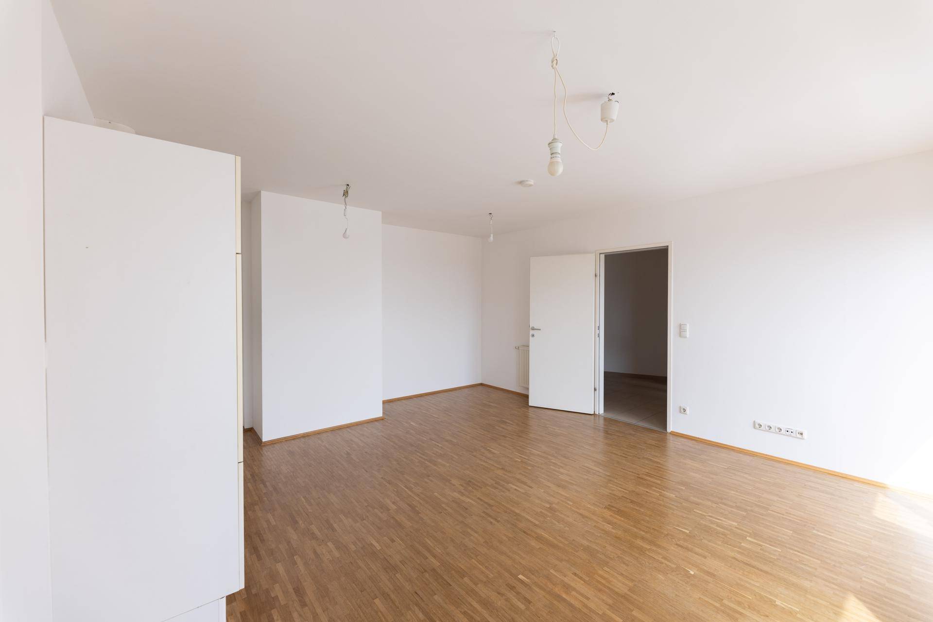 Geräumiges, helles Wohnzimmer mit Parkettboden und weißen Wänden.