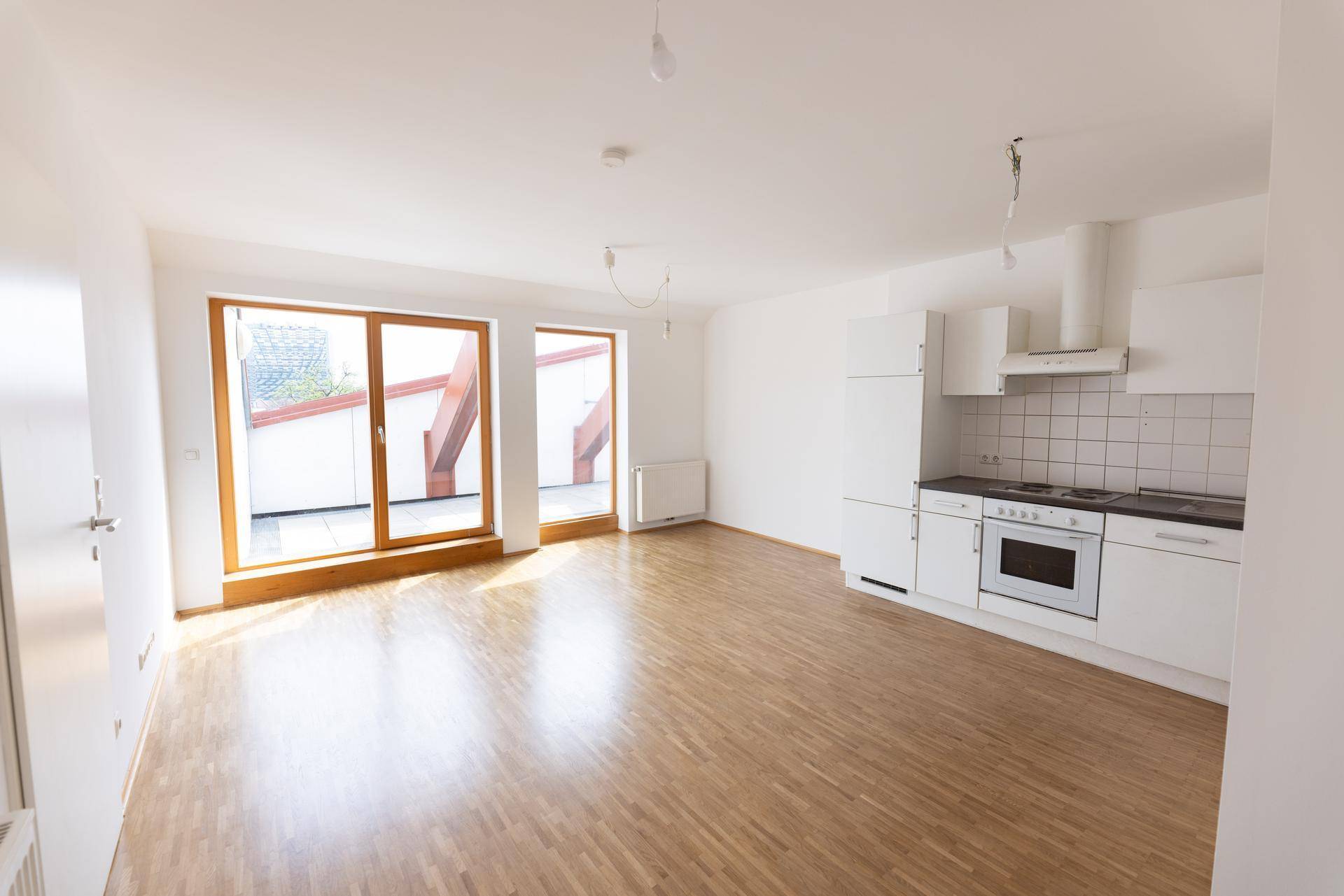 Offener Wohnbereich mit integrierter Küche, Parkettboden und Zugang zur Terrasse.