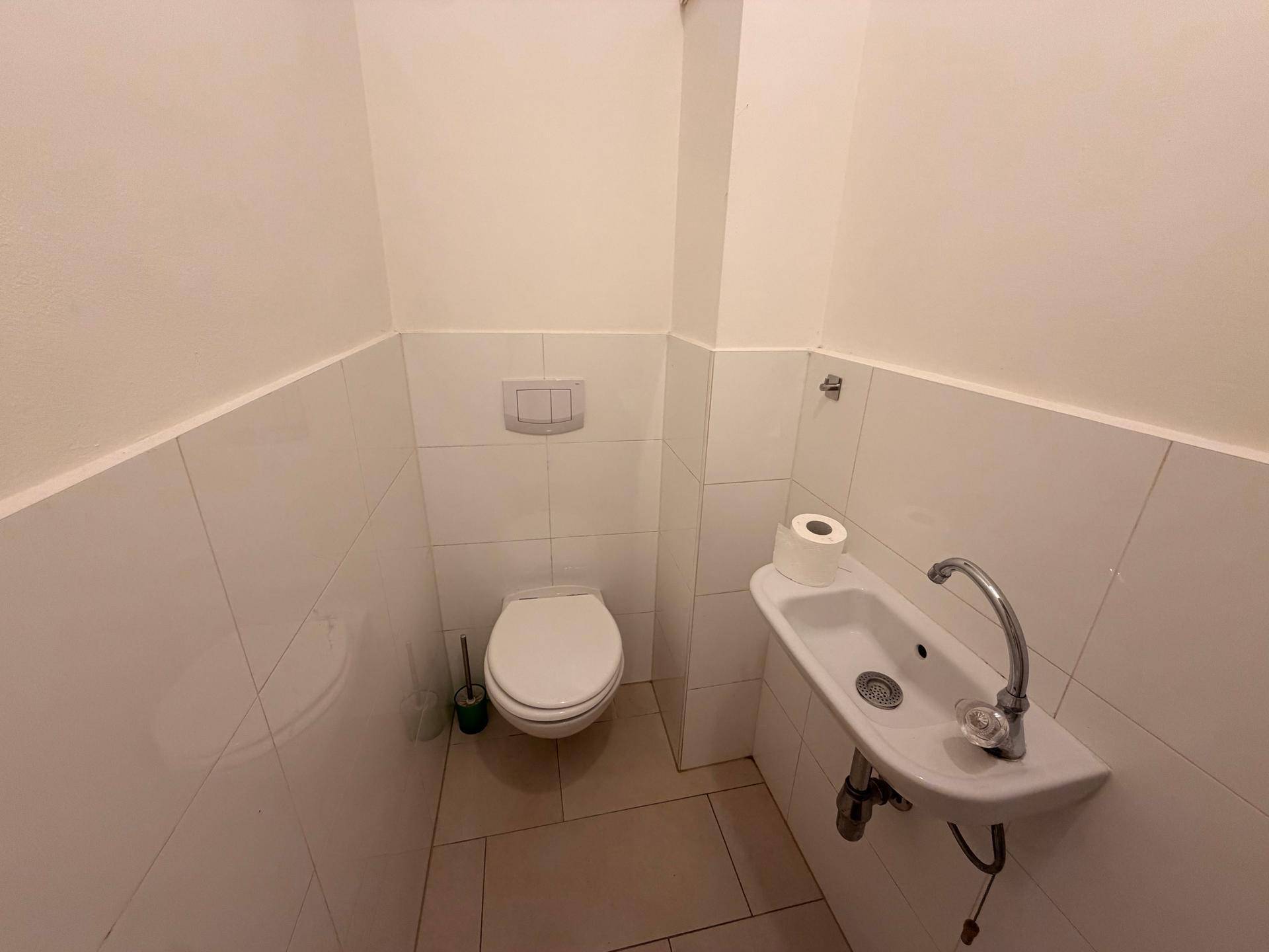 Kleines Gäste-WC mit Wand-WC, Waschbecken und weißen Fliesen an den Wänden.