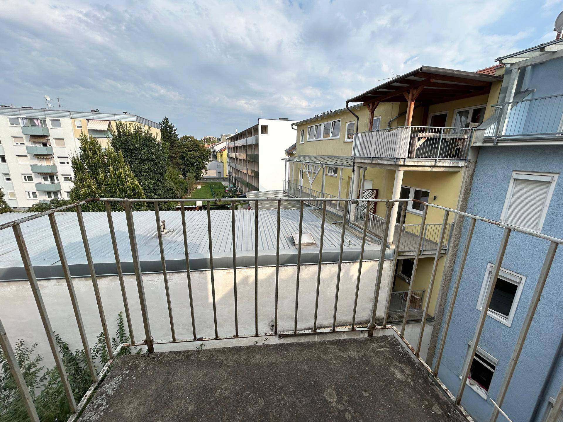 Blick von einem Balkon auf umliegende Gebäude und grüne Bäume.