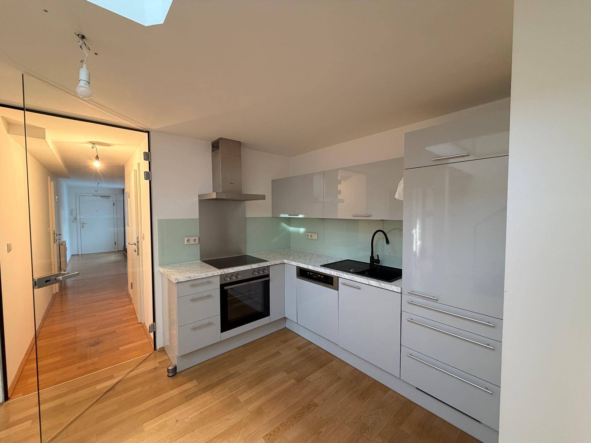 Moderne Küche mit hellgrauen Hochglanzfronten, Induktionskochfeld und Holzboden.