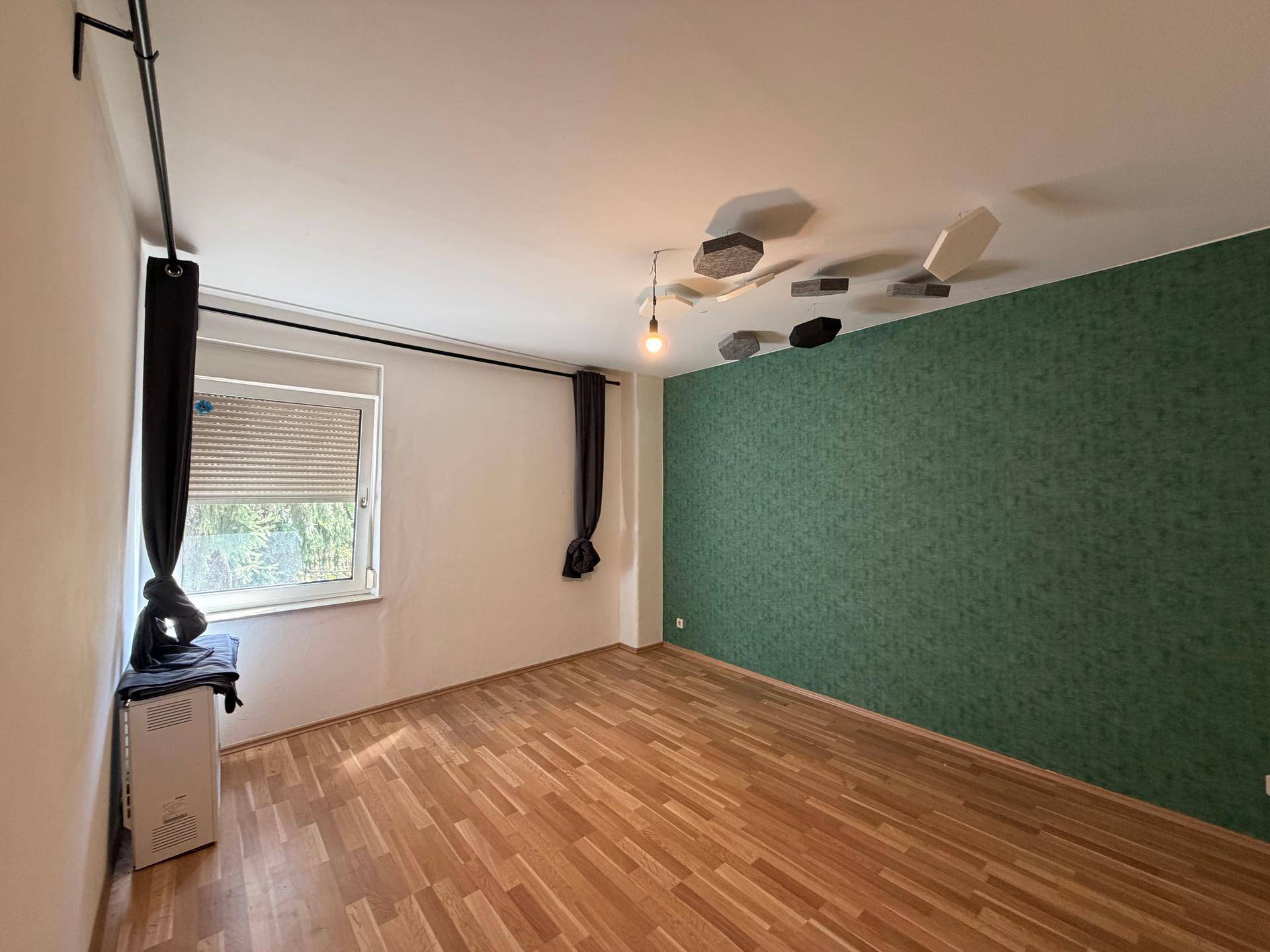 Schlafzimmer mit Laminatboden, einer grünen Akzentwand und einem Fenster mit Rollladen.