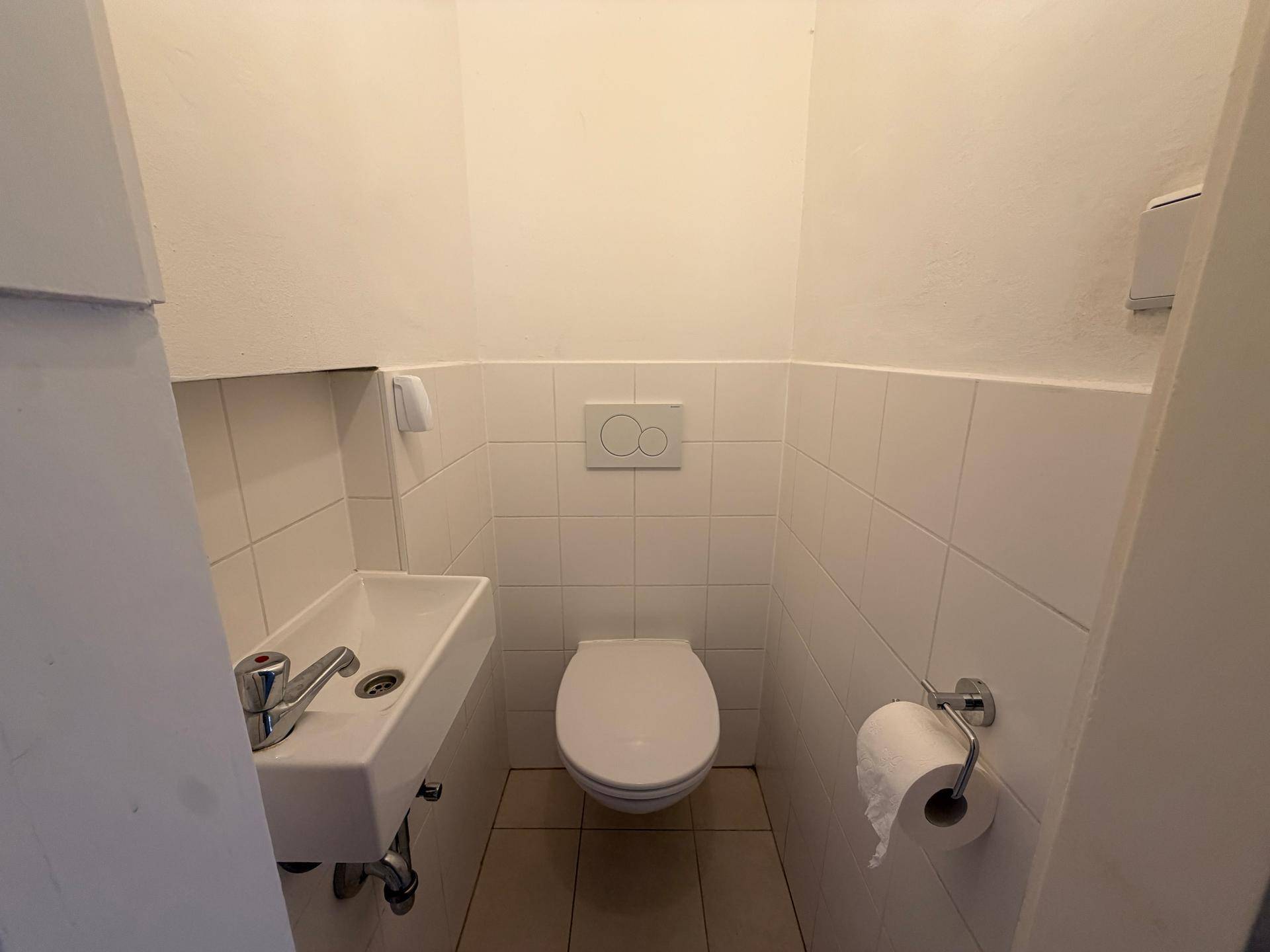 Kleines Gäste-WC mit wandhängendem WC und Handwaschbecken in Weiß.