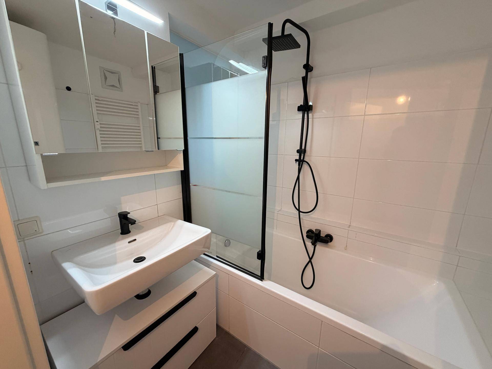 Helles Badezimmer mit Badewanne, moderner Armatur und praktischem Spiegelschrank.
