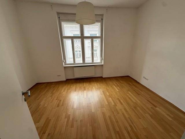 Geräumiger, heller Raum mit Parkettboden und Fenster mit Blick auf die Umgebung.
