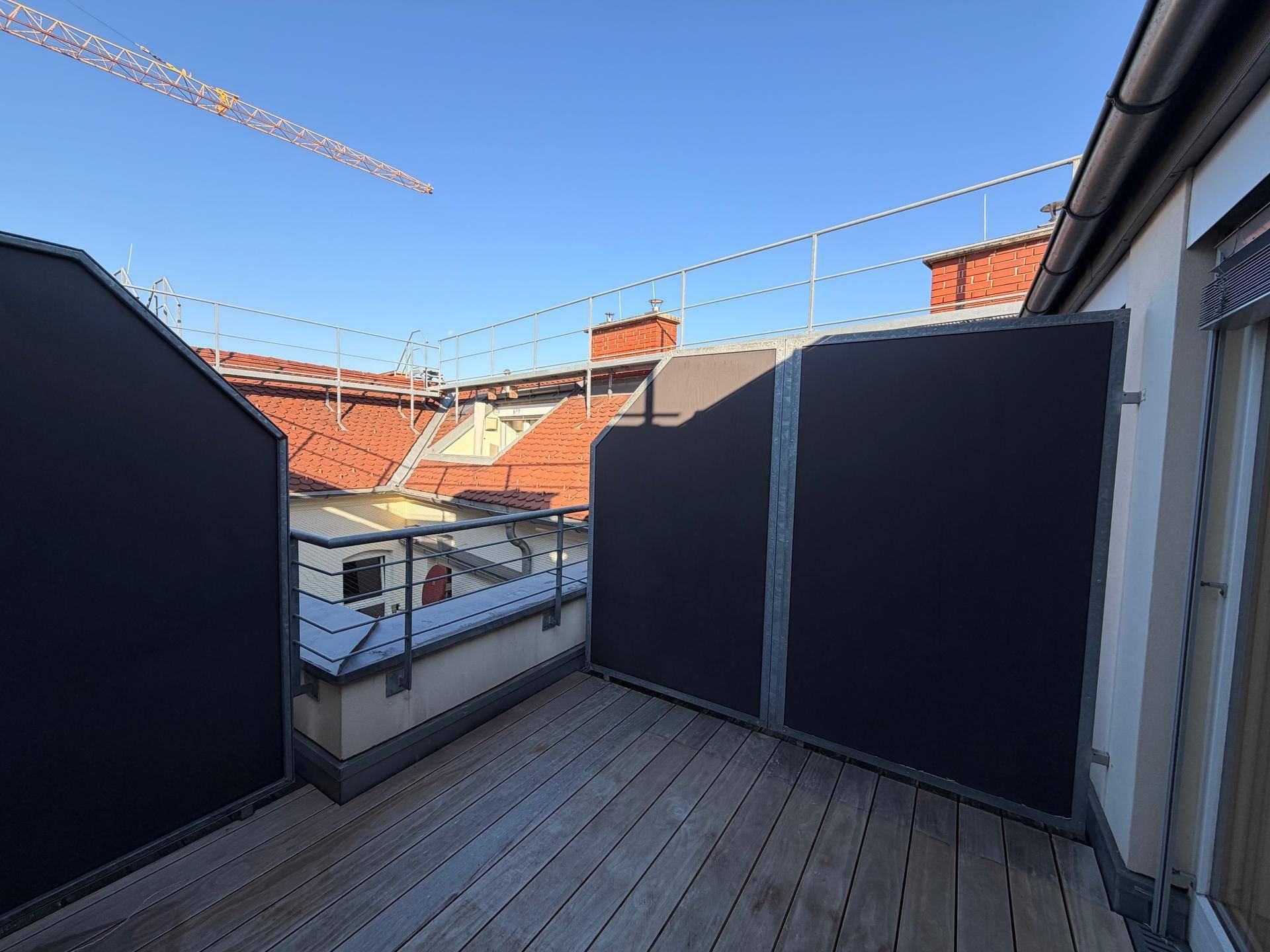 Sonniger Terrassenbereich mit Holzdielen und Sichtschutz, umgeben von traditionellen Dächern.