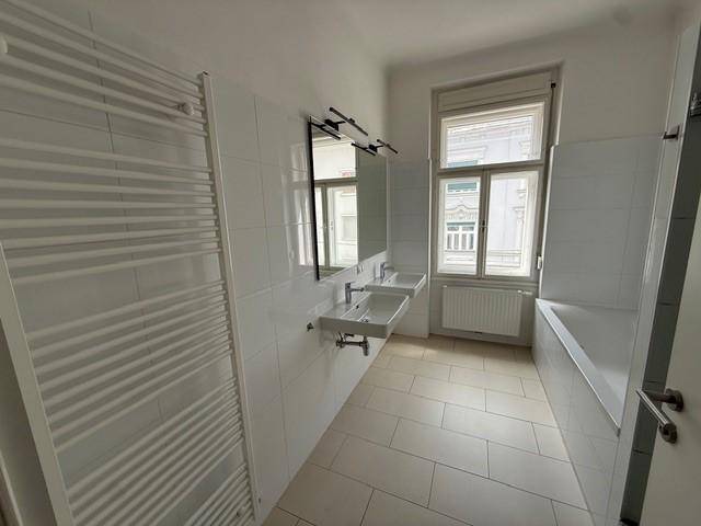 Helles Badezimmer mit Doppelwaschbecken, Badewanne und beheiztem Handtuchhalter.