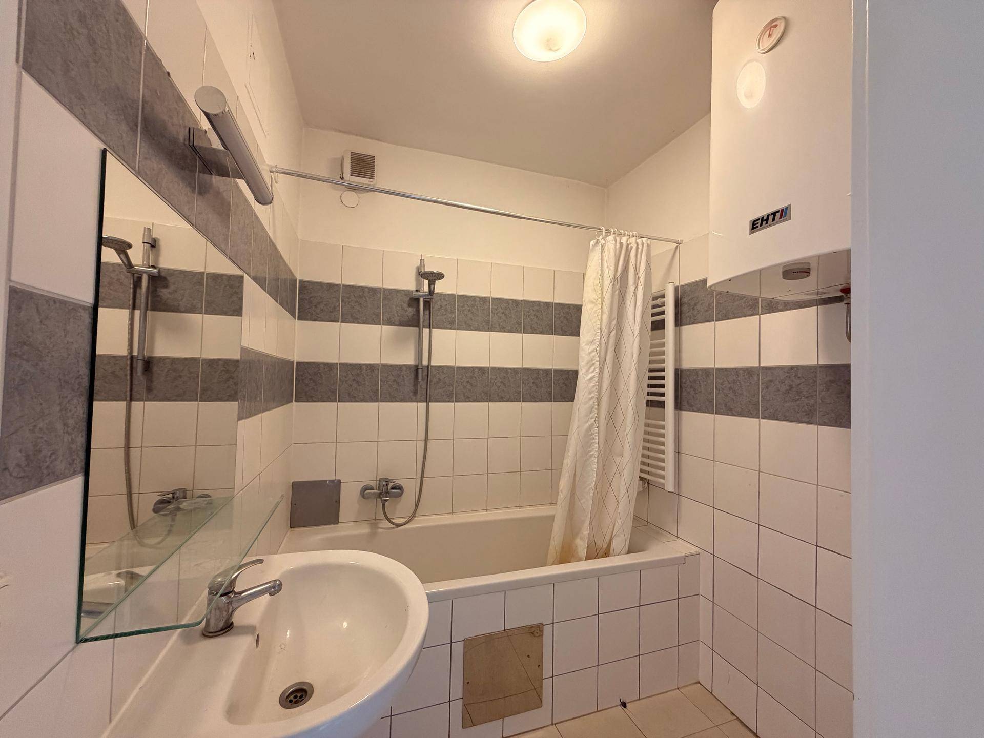 Funktionales Badezimmer mit Badewanne, Waschbecken und Fliesen in Weiß und Grau.