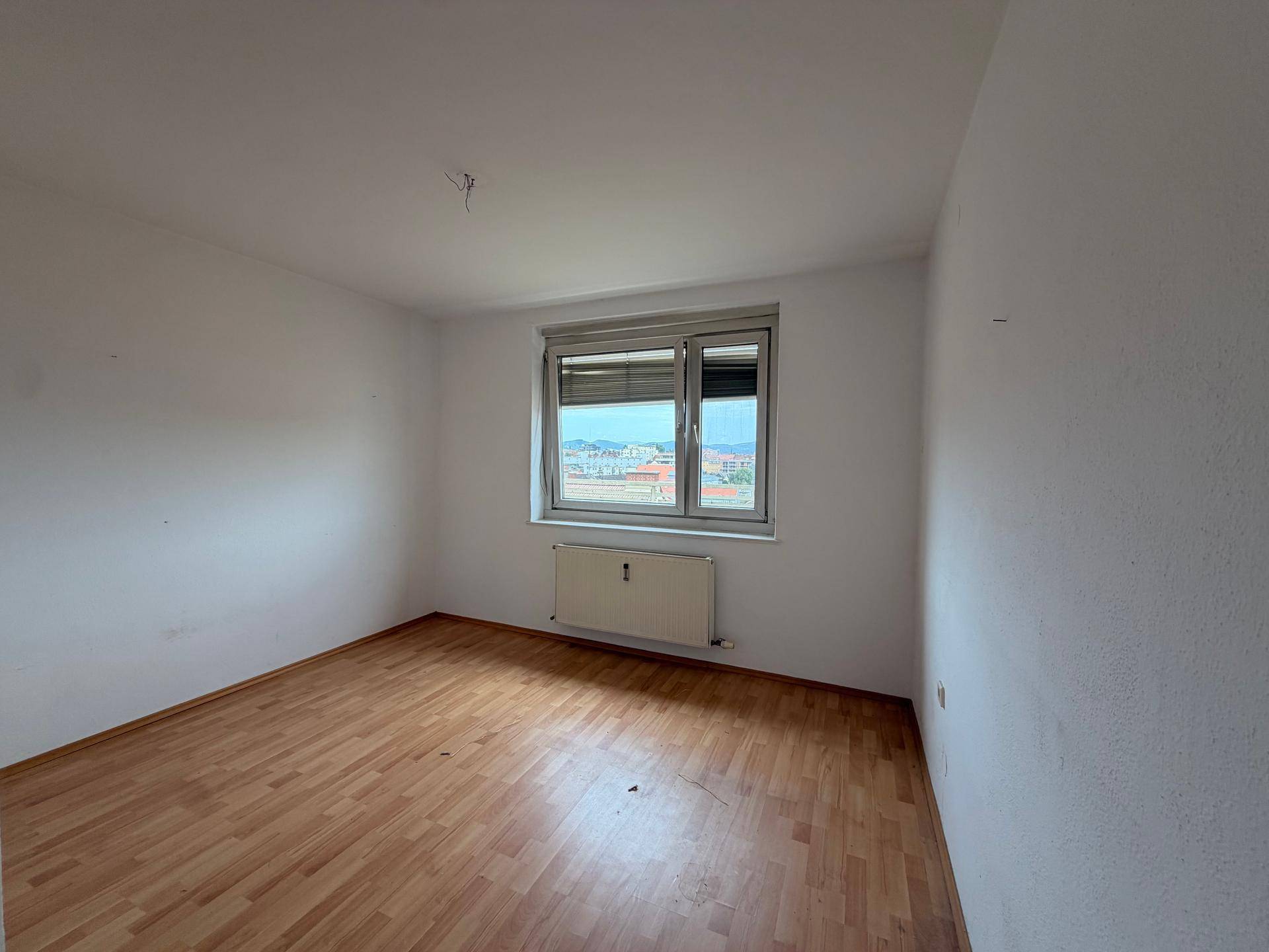 Helles Zimmer mit Parkettboden und Heizkörper unter dem Fenster mit Weitblick.