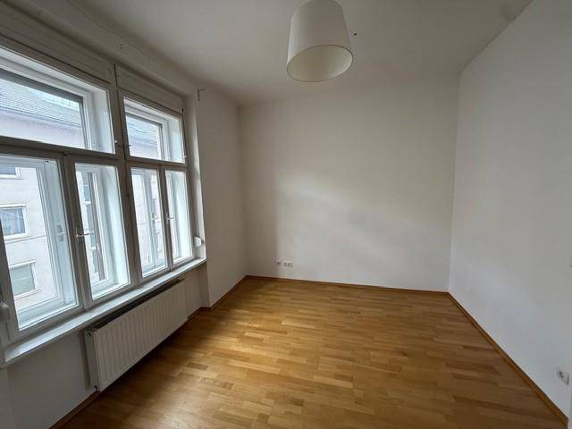 Heller Raum mit Parkettboden und breitem Fenster, das viel Tageslicht hereinlässt.