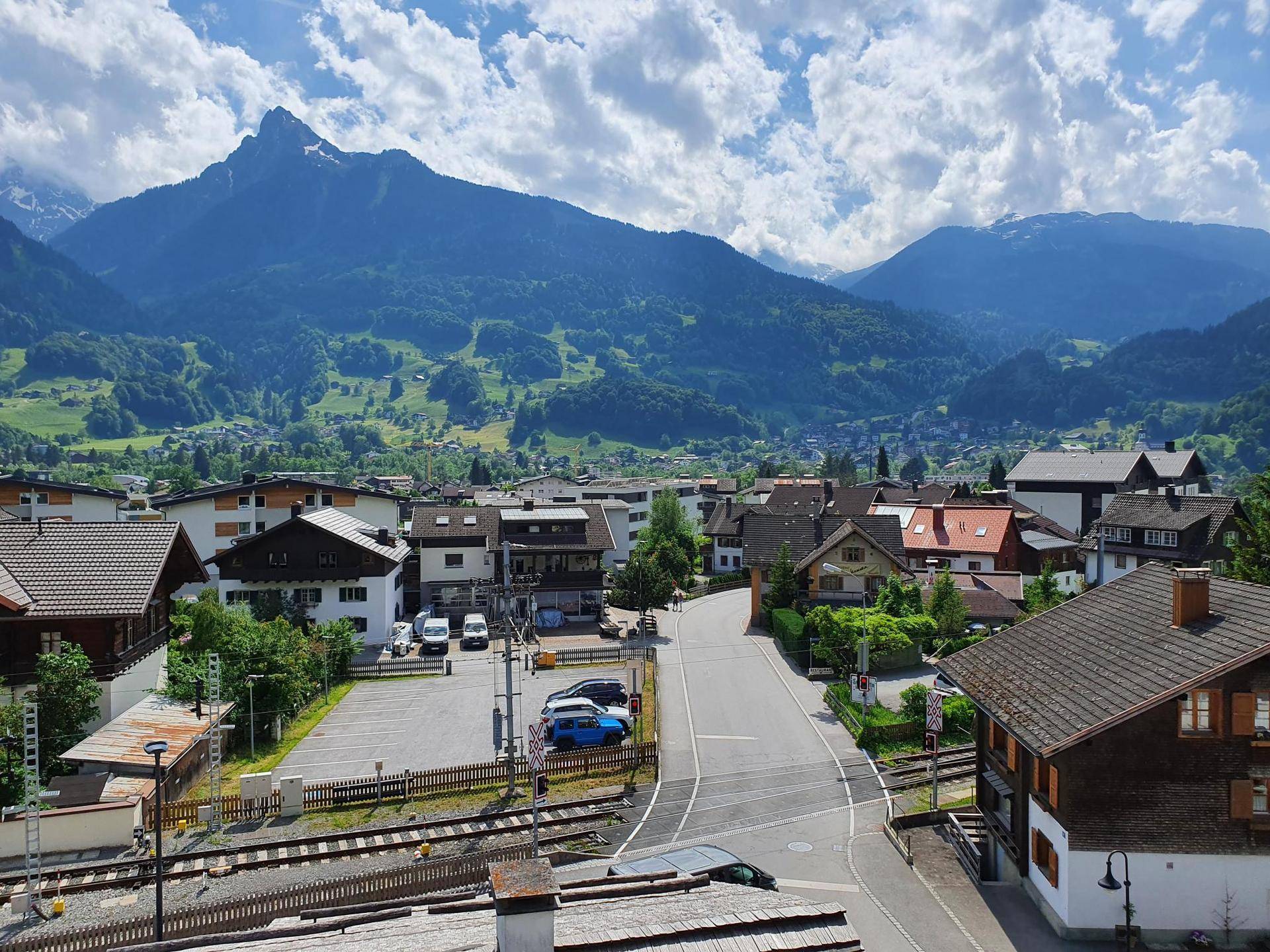 Panoramablick über eine malerische Stadt im Tal, umgeben von majestätischen Bergen unter bewölktem Himmel.