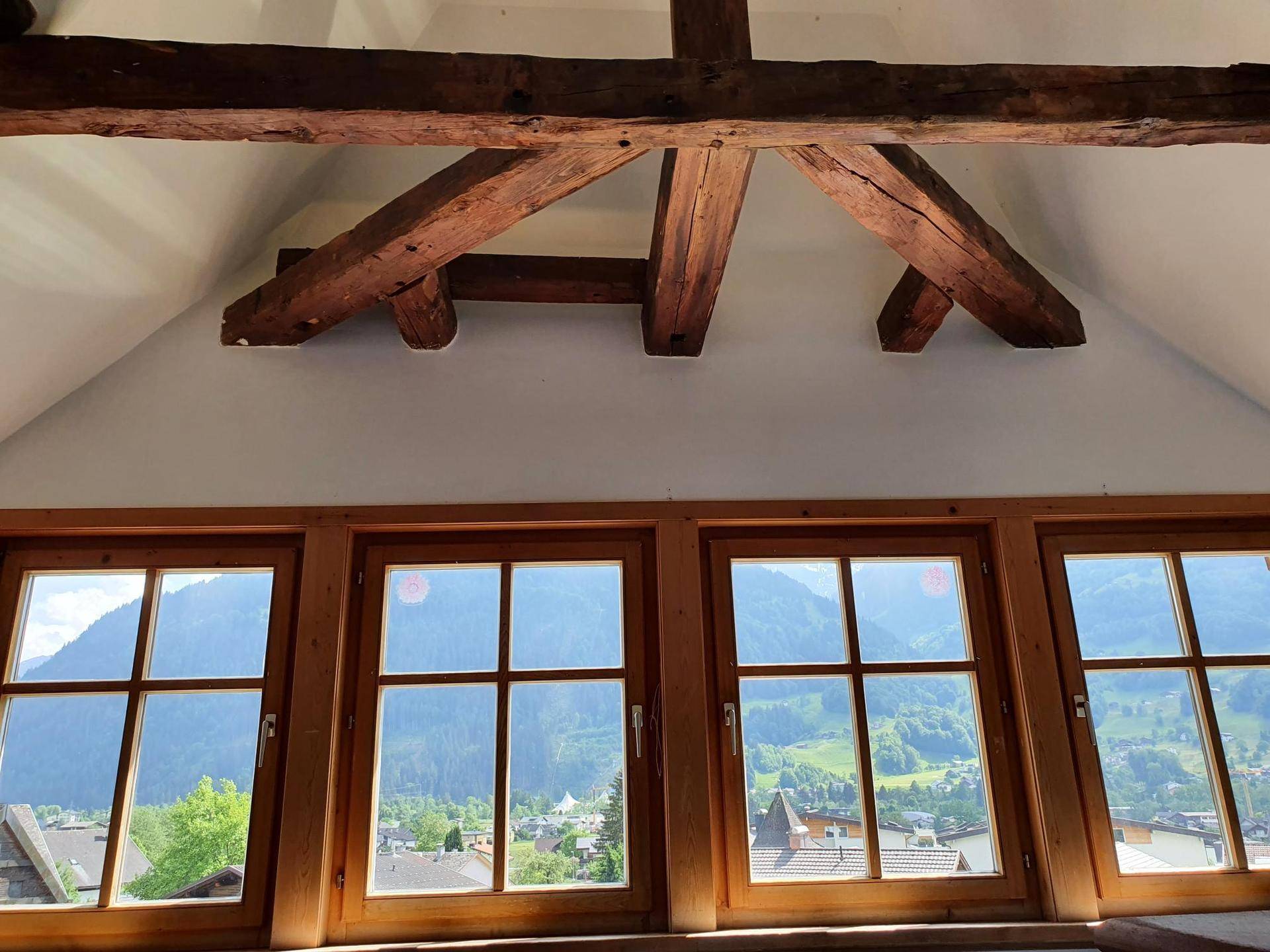 Große Fensterfront mit Holzbalken und einem weiten Blick auf die umliegende Berglandschaft.