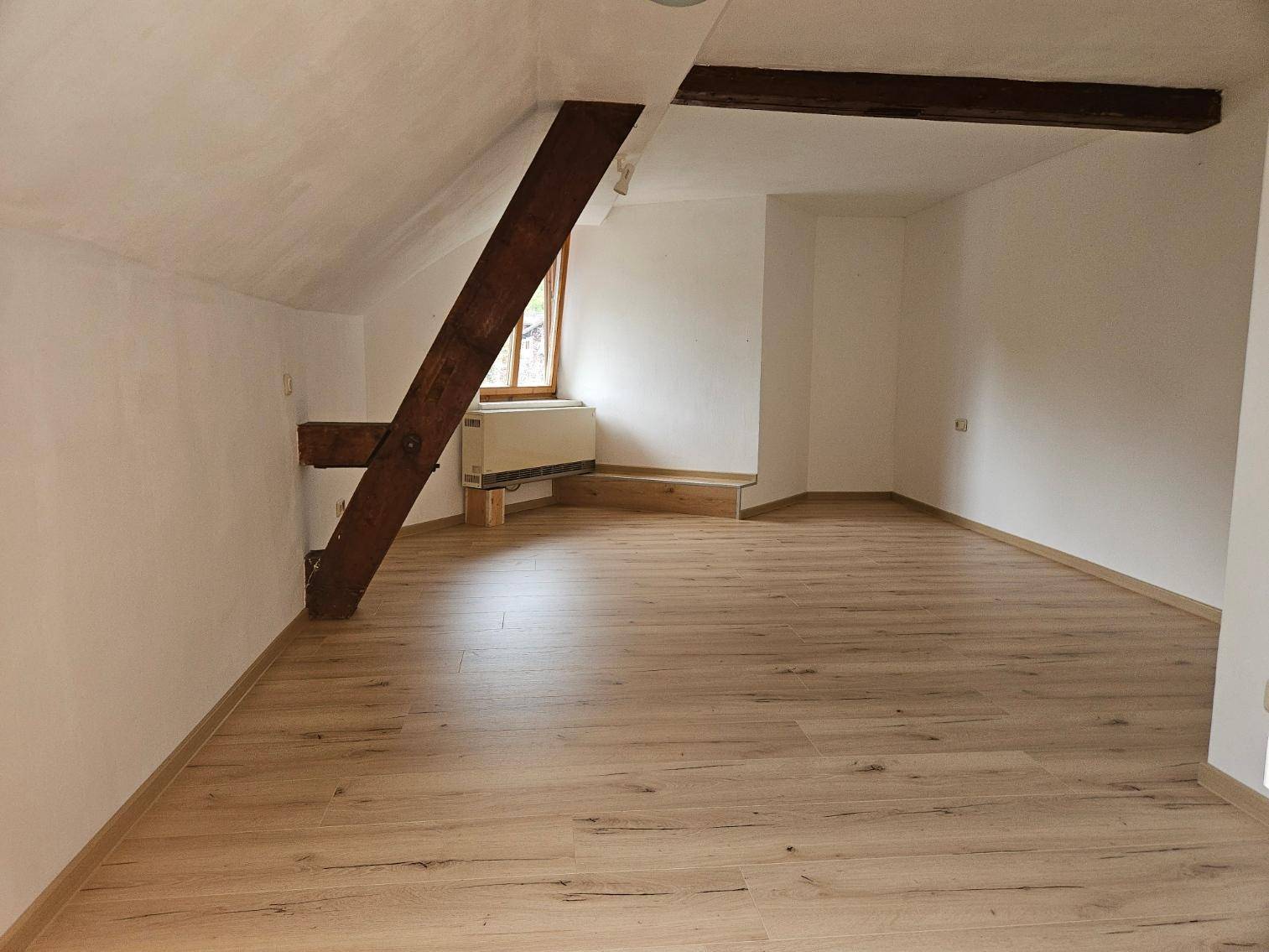 Heller Dachraum mit sichtbaren Holzbalken und neuem Laminatboden, bereit zur individuellen Gestaltung.