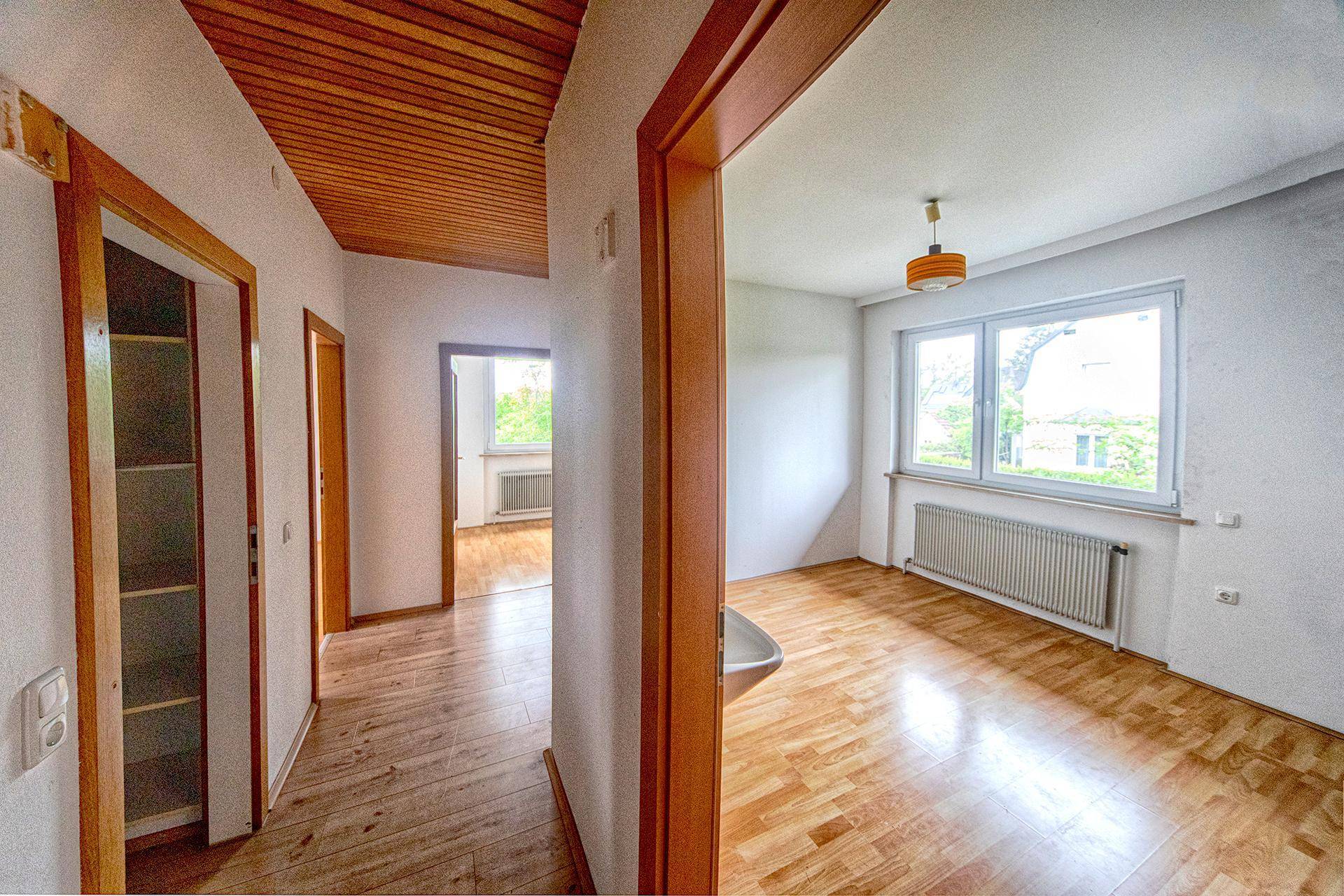 Langer Flur mit Holzdeckenverkleidung und Parkettboden, der zu hellen Zimmern mit Fenstern führt.
