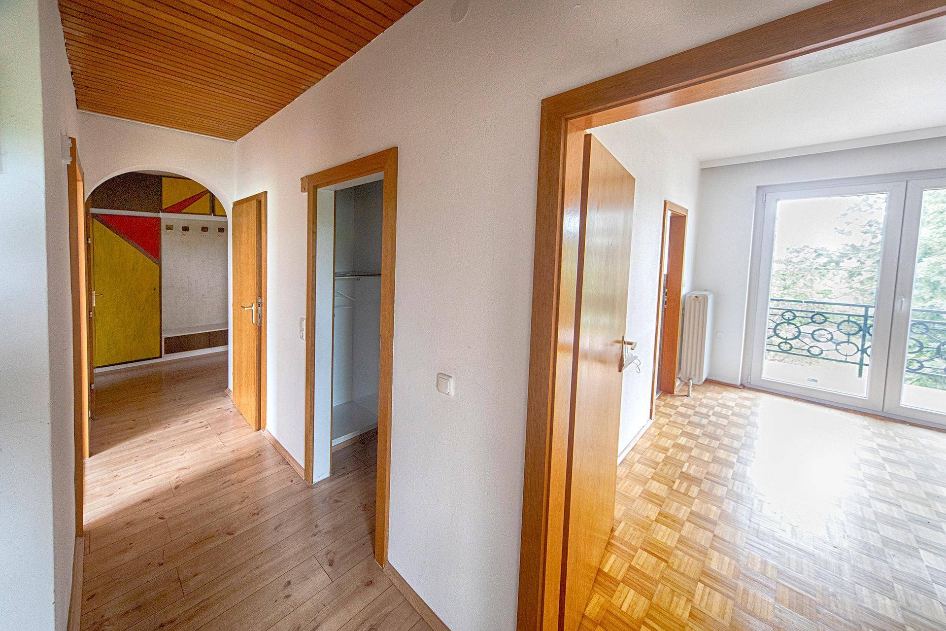 Heller Flur mit Holzdeckenverkleidung, Parkettboden und Zugang zu weiteren Räumen und einem Balkon.