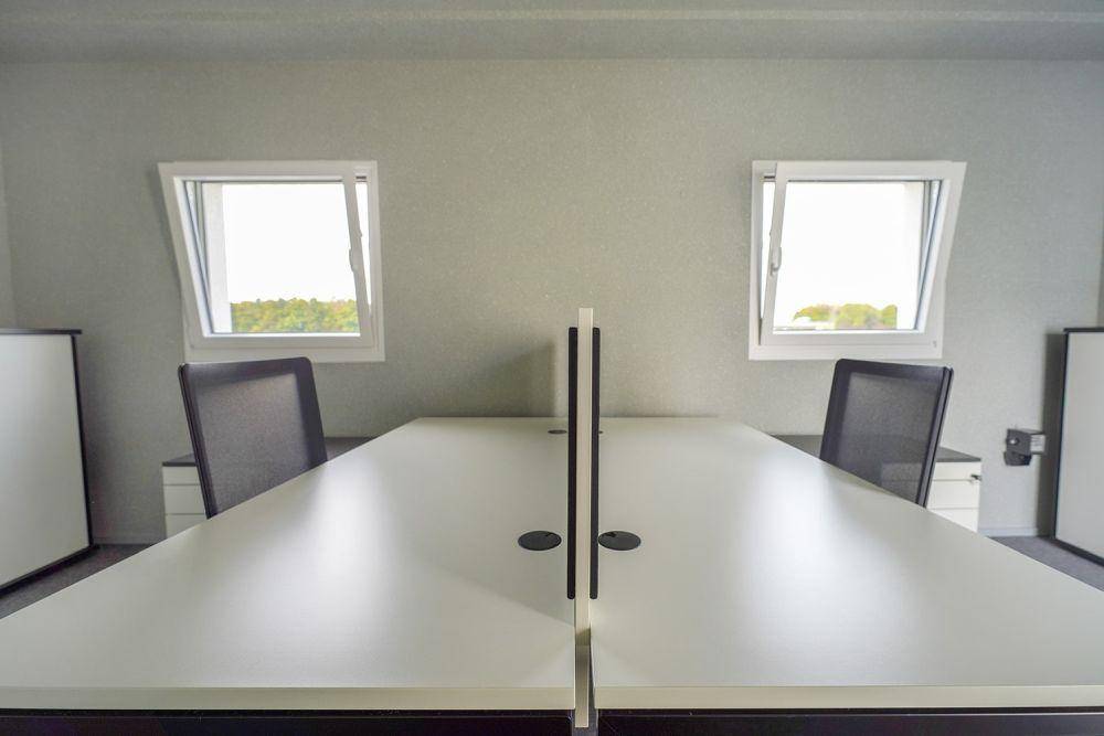 Heller Büroraum mit zwei Schreibtischen, Bürostühlen und geöffneten Fenstern für frische Luft und eine weite Aussicht.