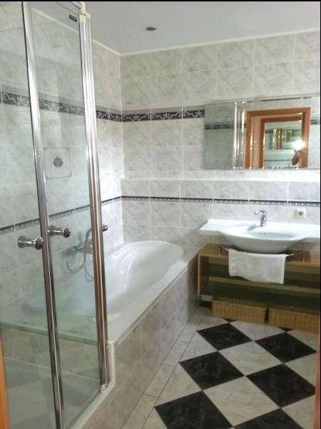 Gefliestes Badezimmer mit Badewanne, Duschkabine und Schachbrettmuster auf dem Boden.