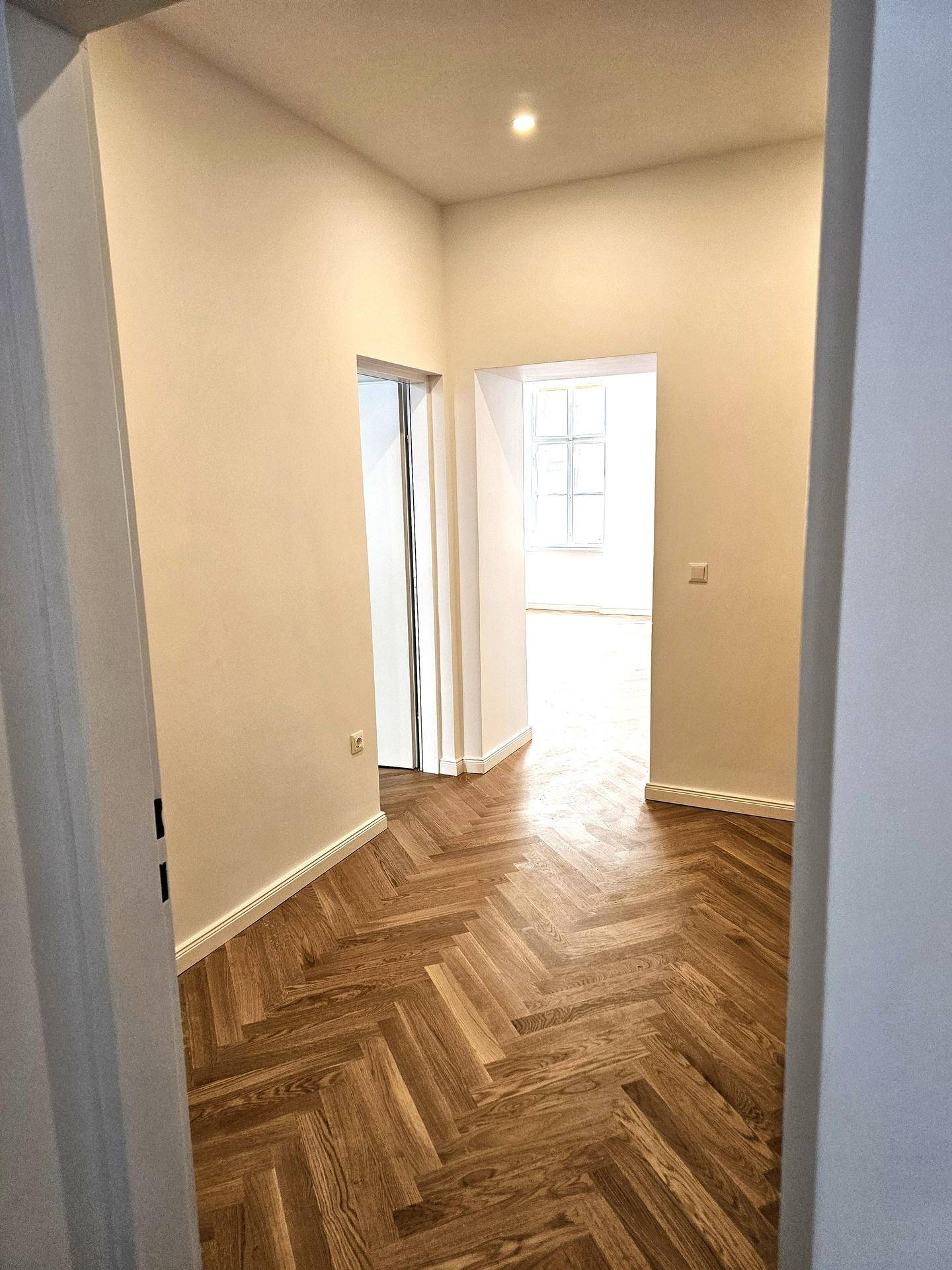Heller Flur mit Fischgrätparkett, der zu weiteren Räumen der Wohnung führt und gut gepflegt ist.