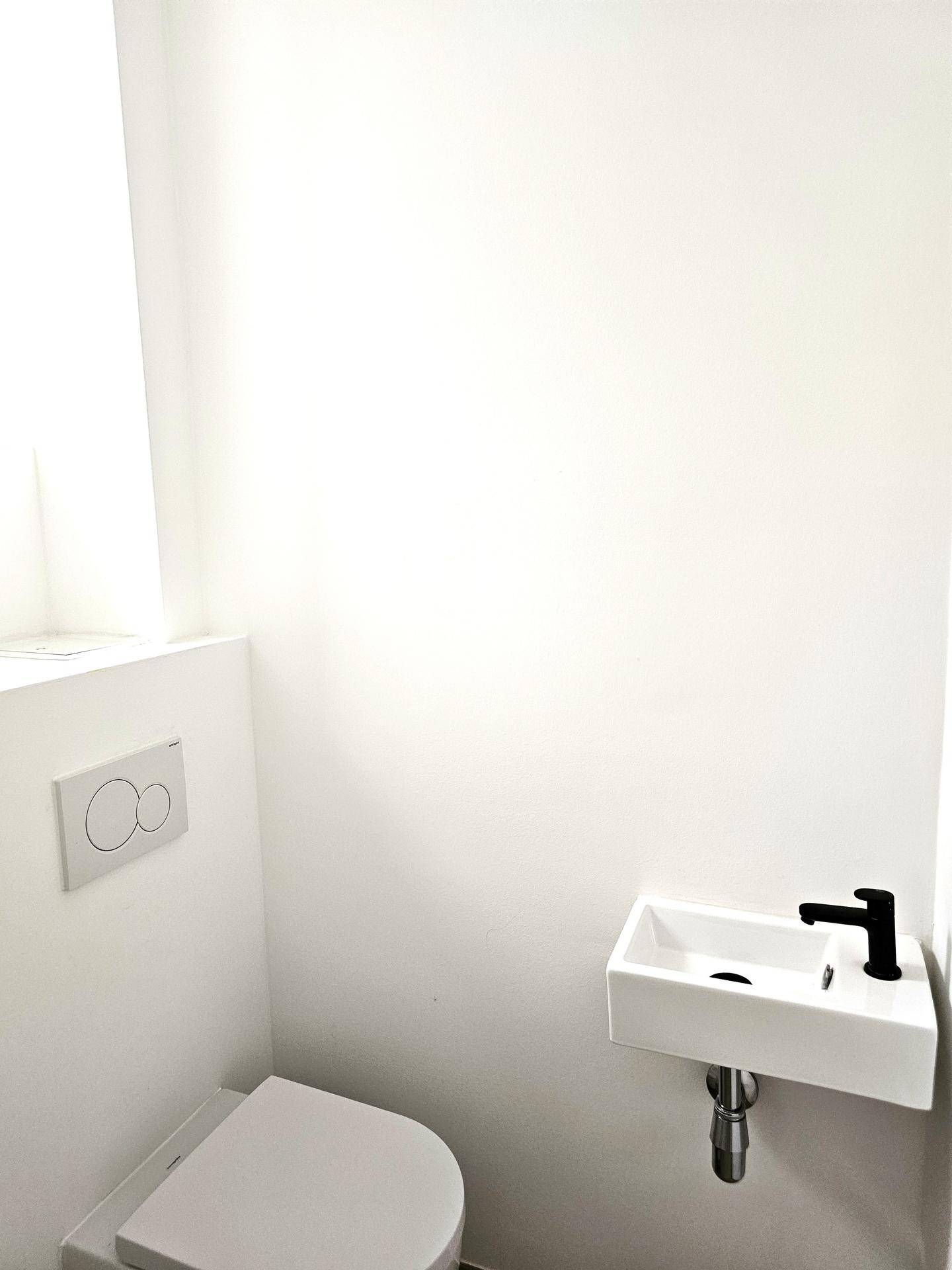 Modernes Gäste-WC mit wandhängender Toilette und kleinem Waschbecken in minimalistischem Design.