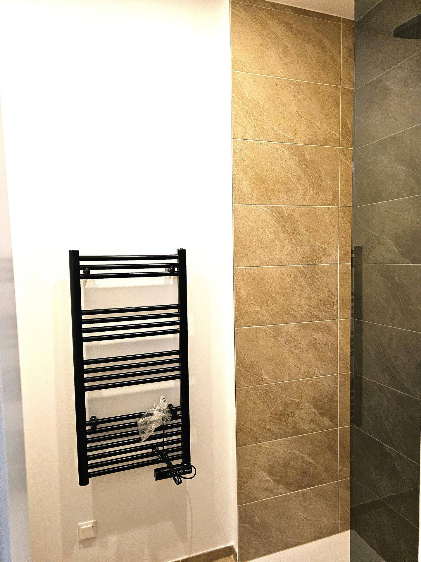 Modernes Badezimmer mit beheiztem Handtuchhalter und elegant gefliester Duschwand, in gehobener Ausstattung.