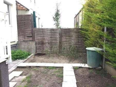 Kleiner Hinterhof mit gepflastertem Weg, Zaun und Grünflächen.