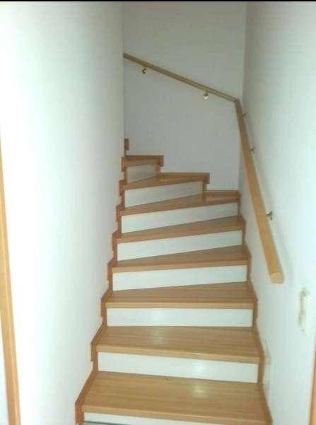Holztreppe mit weiß gestrichenen Setzstufen und Handlauf in einem hellen Flur.