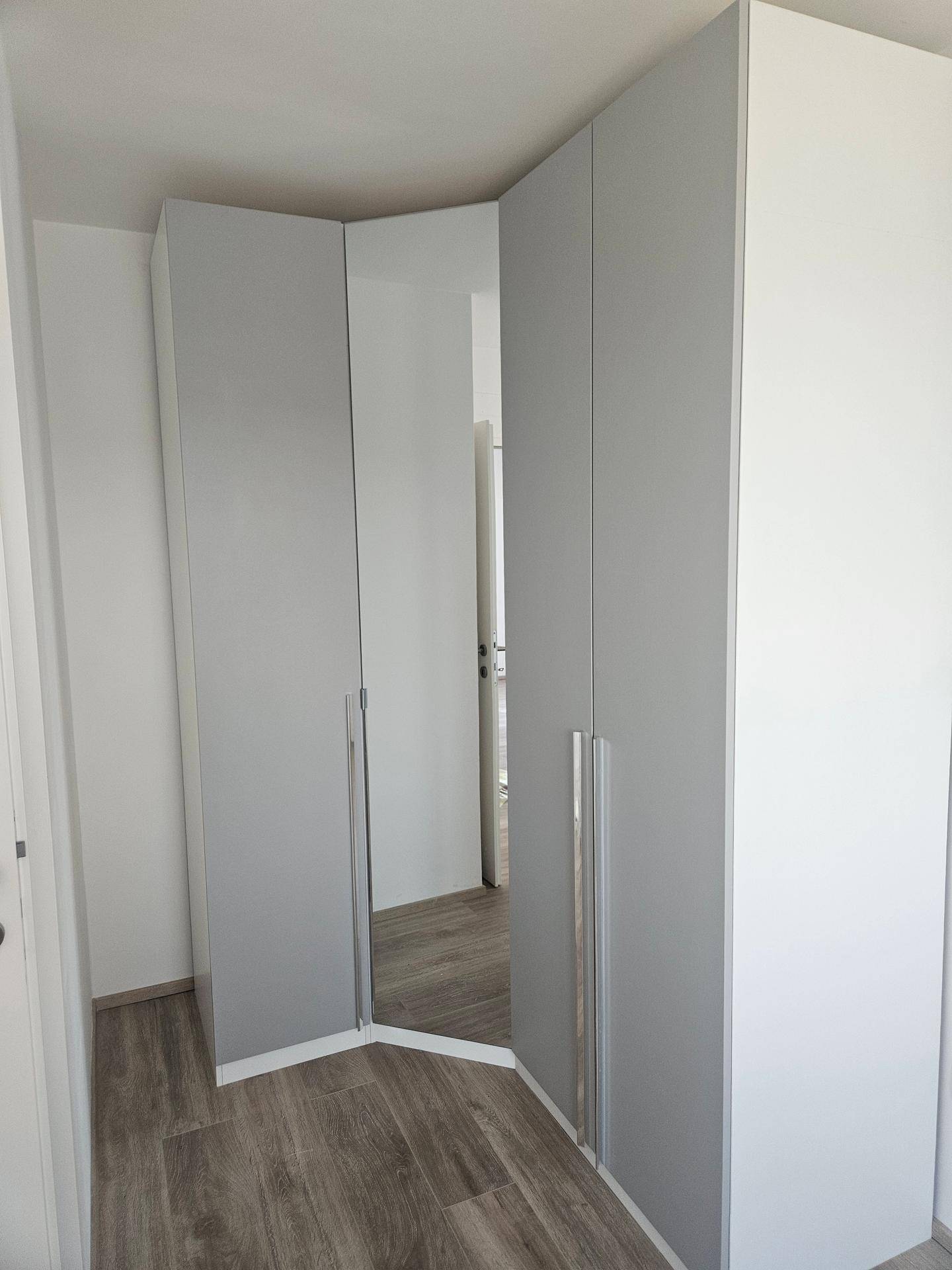 Moderner Eckkleiderschrank in Weiß und Grau mit Spiegeltür und Laminatboden im Schlafzimmer.