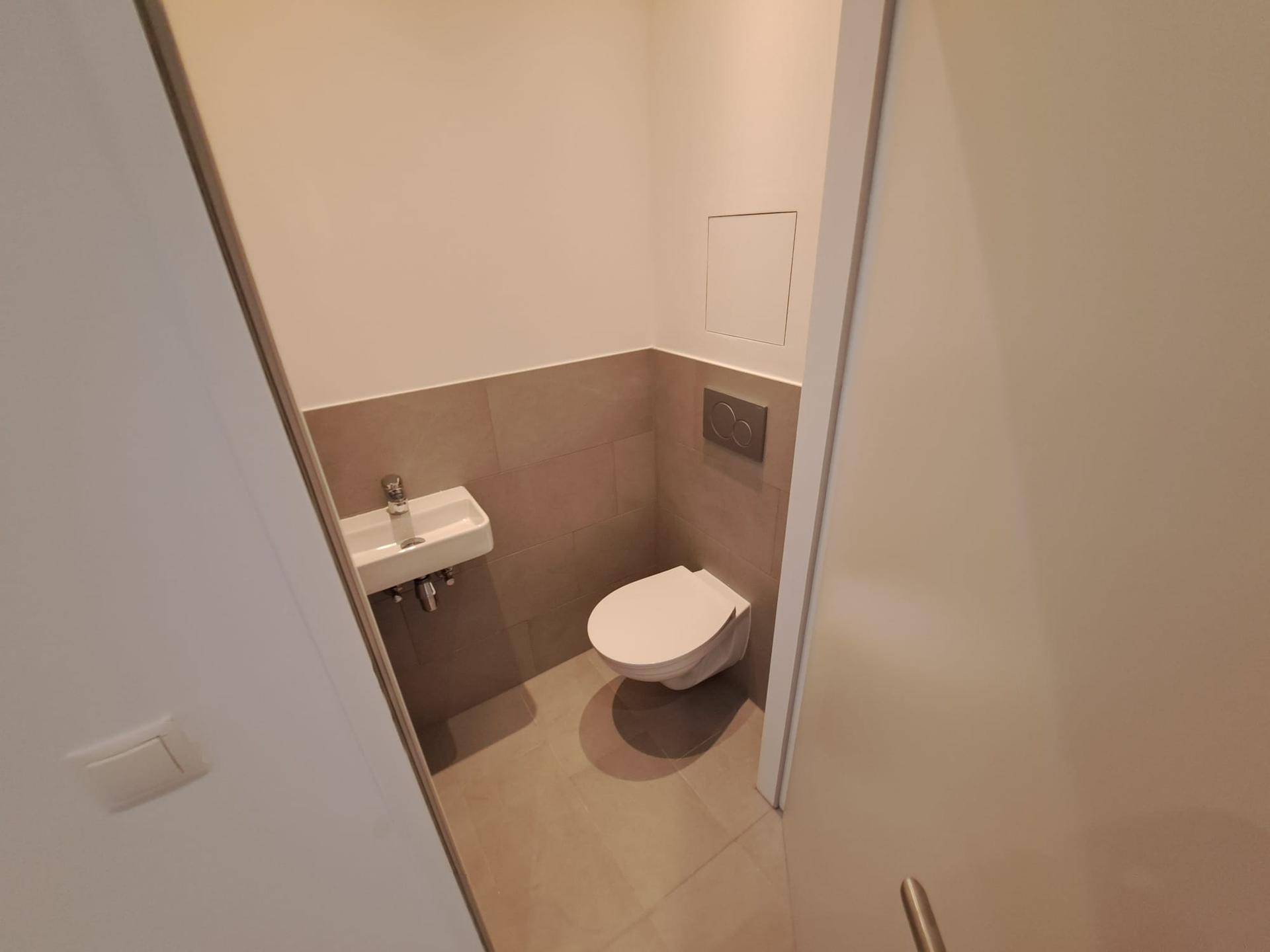 Kleines Gäste-WC mit wandhängender Toilette und kompaktem Waschbecken, modern gefliest.