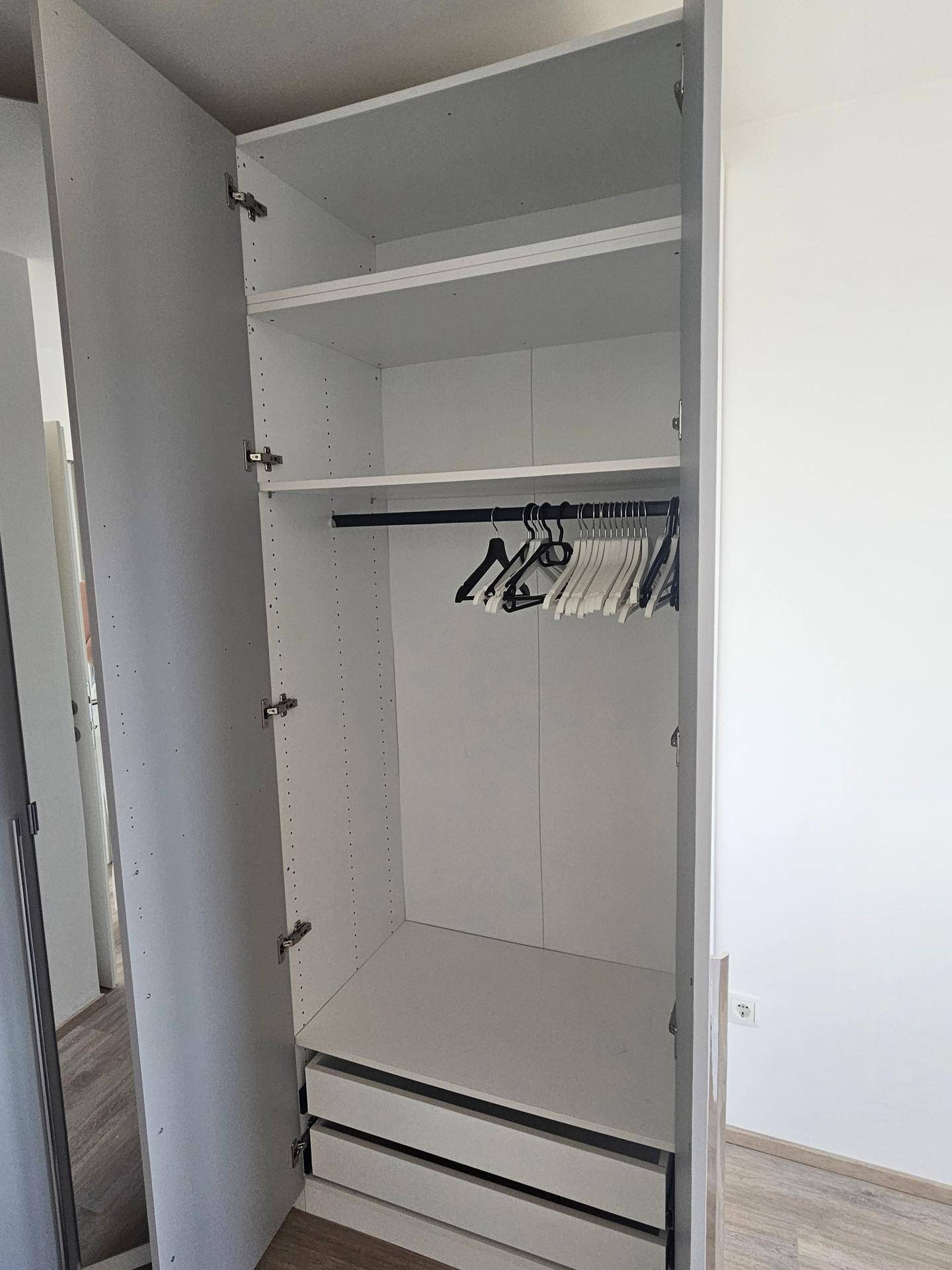 Innenansicht eines weißen Kleiderschranks mit Regalen, Kleiderstange und Schubladen für optimale Organisation.