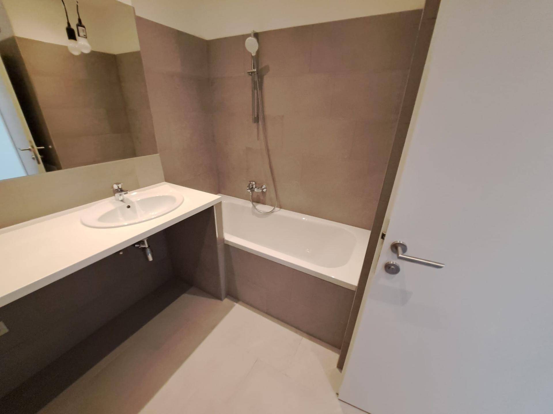 Badezimmer mit Badewanne inklusive Duschfunktion, Waschtisch und großem Spiegel, modern gefliest.
