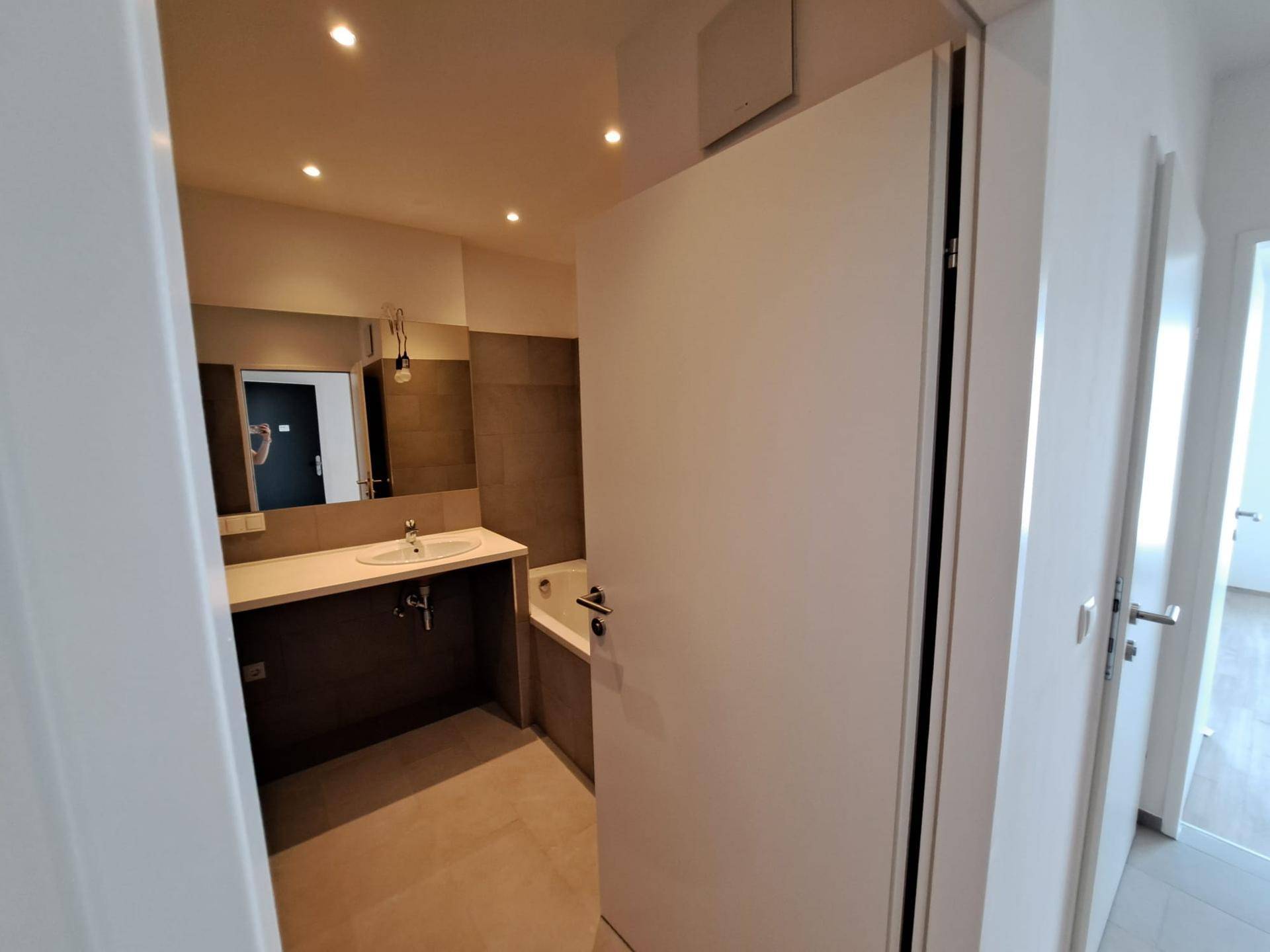 Modernes Badezimmer mit Waschtisch, Spiegel und einer Eckbadewanne, hell gefliest.