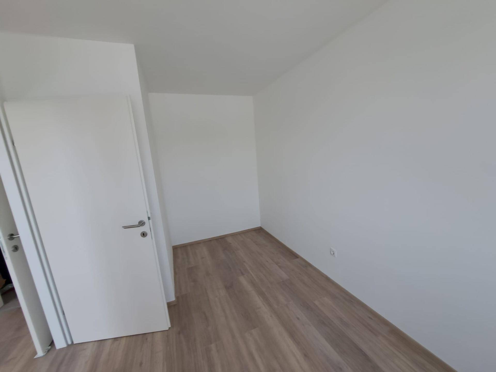 Leeres Zimmer mit hellem Laminatboden und weißen Wänden, bereit zum Einrichten.