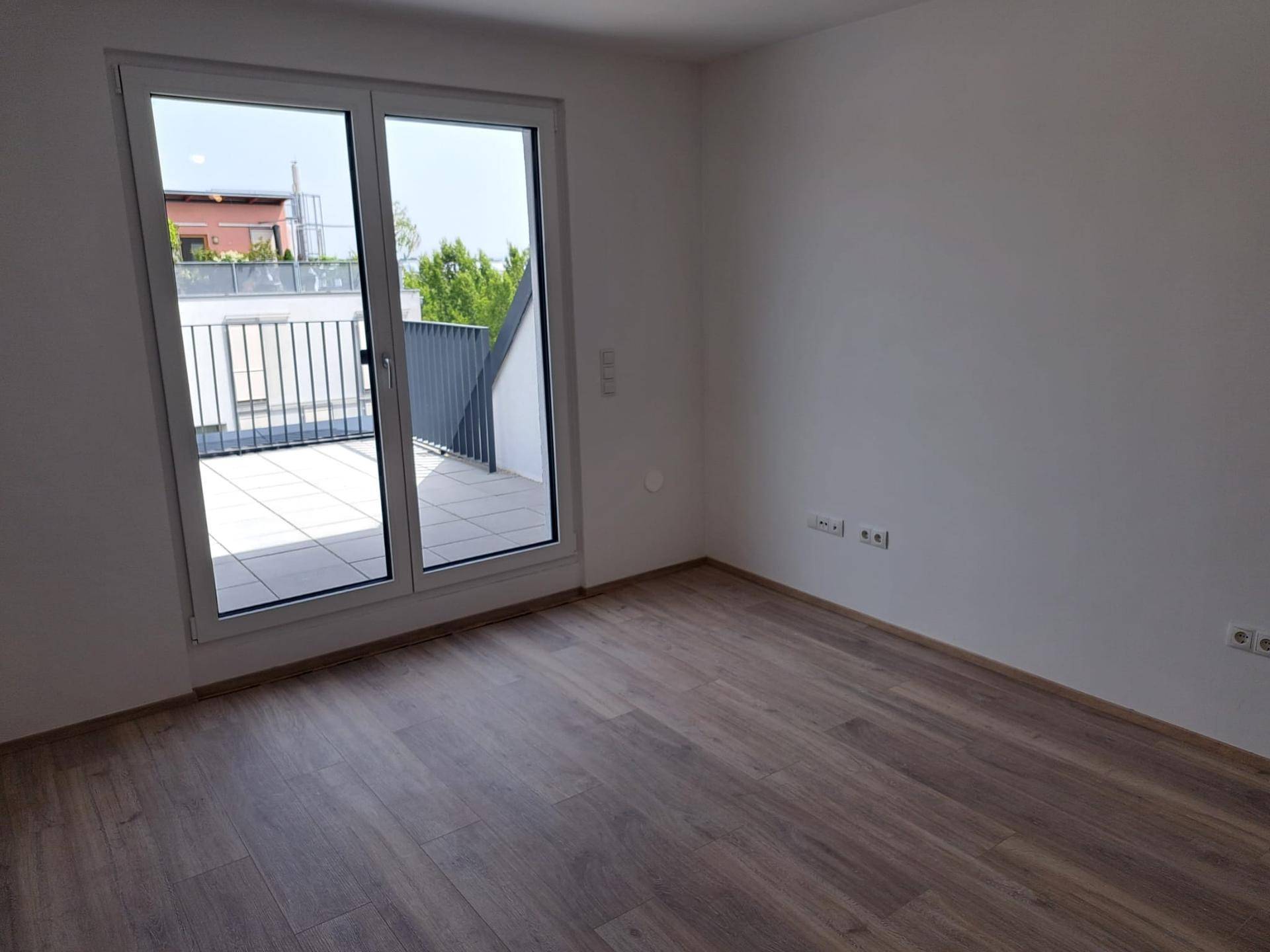 Helles Schlafzimmer mit Laminatboden und großem Schiebetürzugang zu einer sonnigen Terrasse.