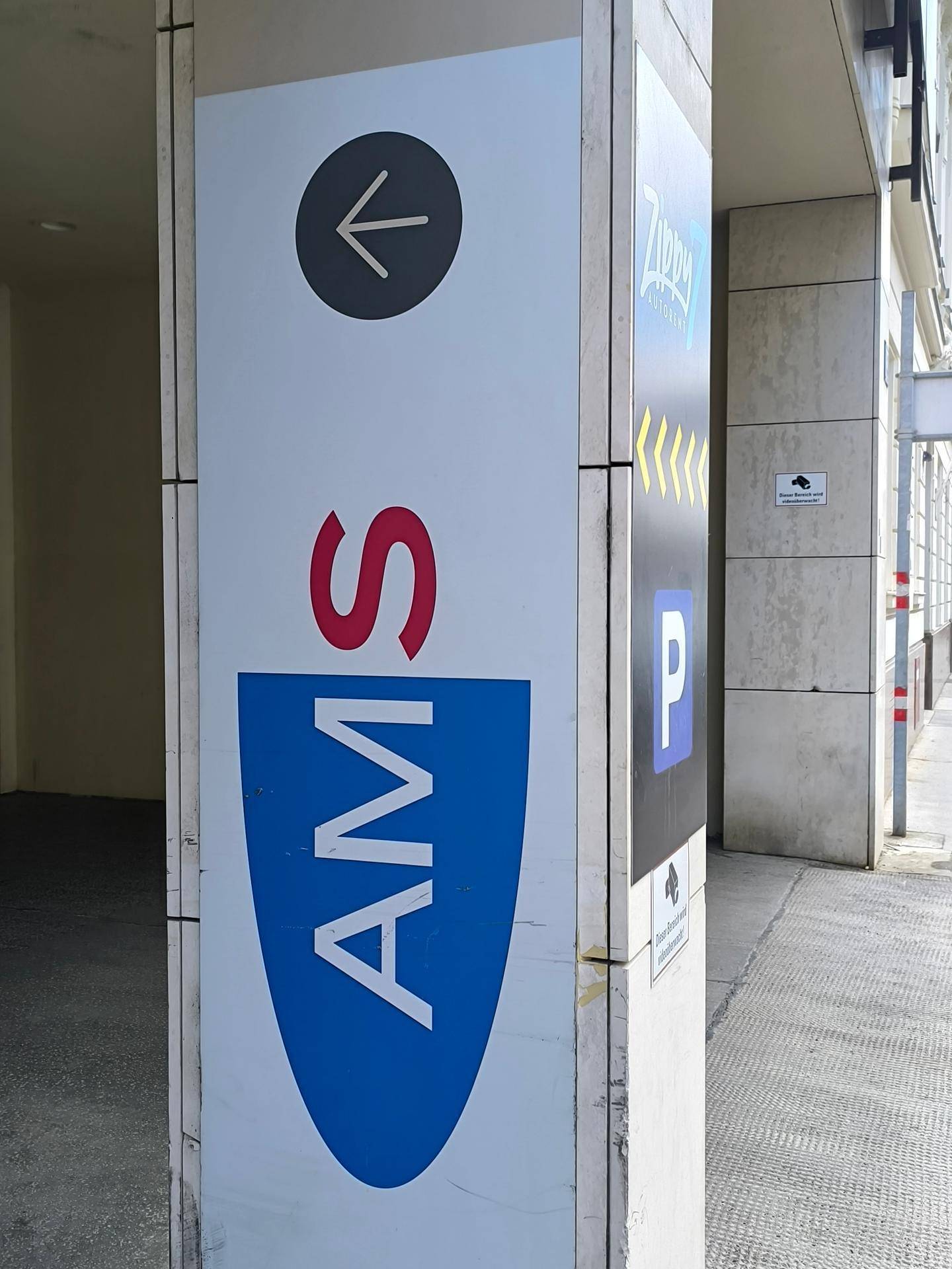 Beschilderung für eine Tiefgarage mit Pfeil und Logo an einem modernen Gebäudepfeiler.