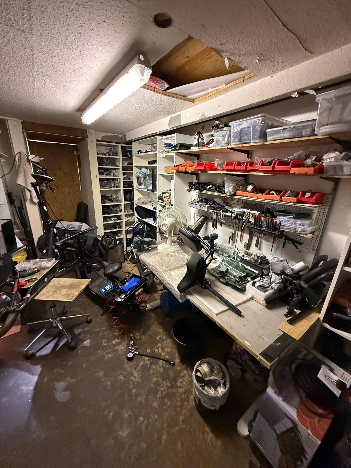 Unaufgeräumter Werkstattraum mit Werkzeugen, Ersatzteilen und E-Scootern zur Reparatur.